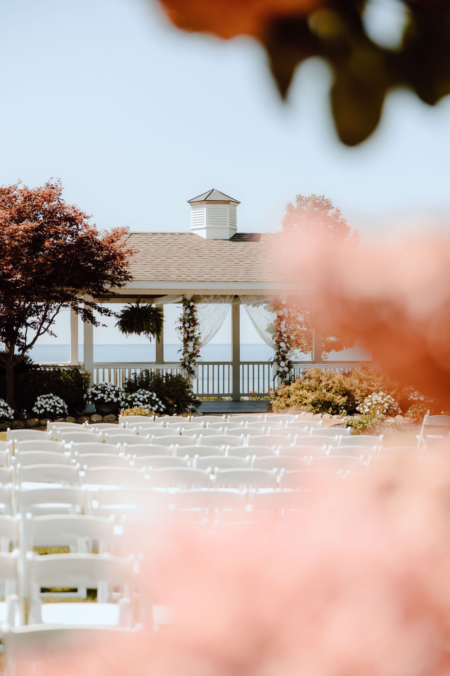 Elegant outdoor wedding ceremony setup with white chairs facing a gazebo overlooking the water.