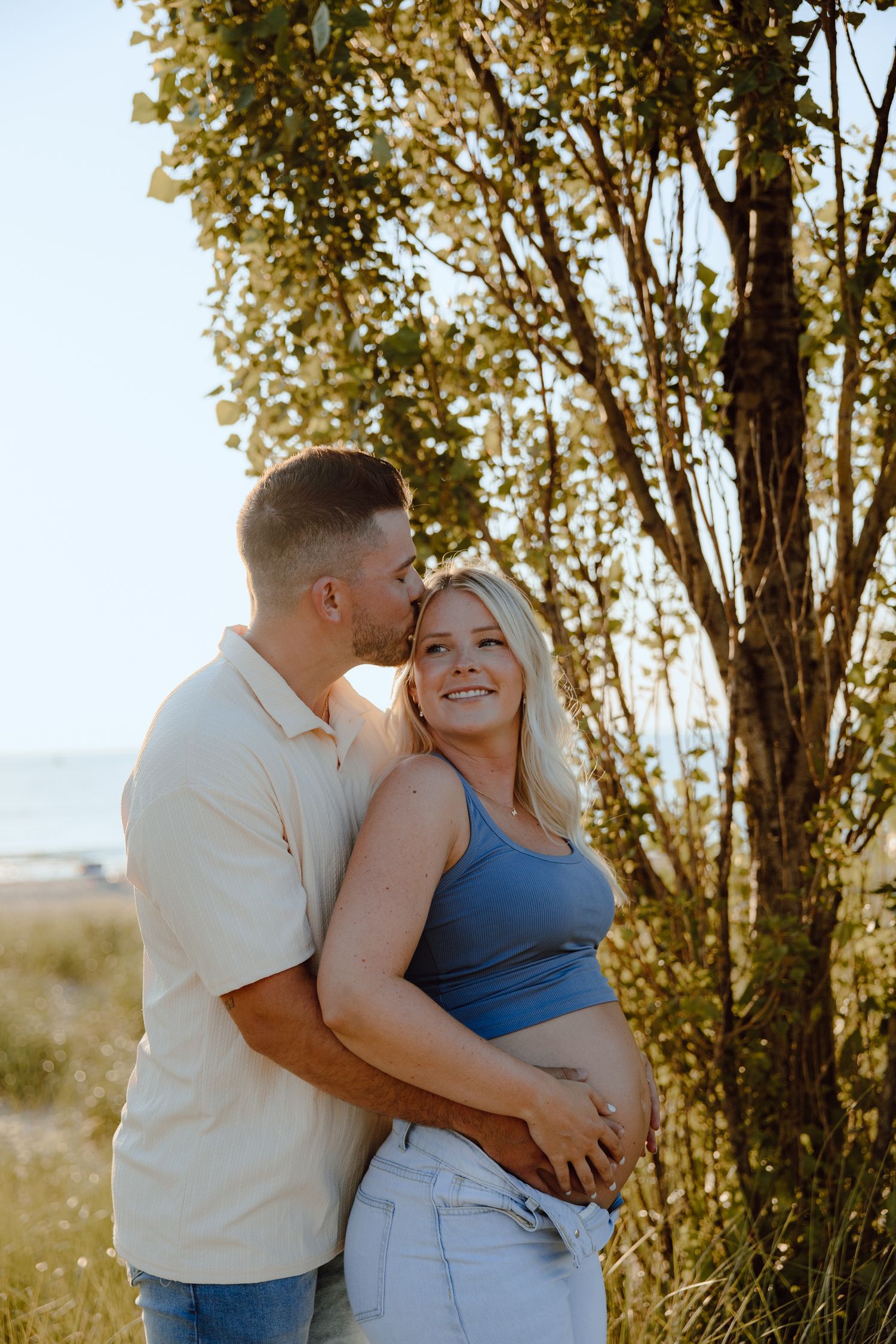Couple shares intimate moment among sunlit trees during outdoor photo session.