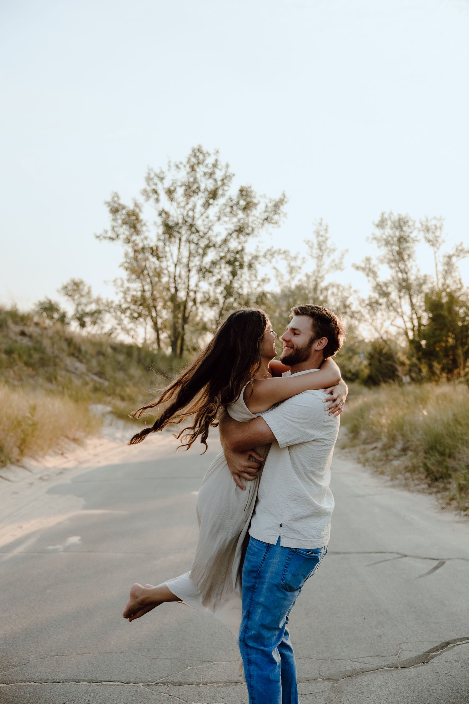 Playful couple sharing a romantic moment on a sandy path during sunset.