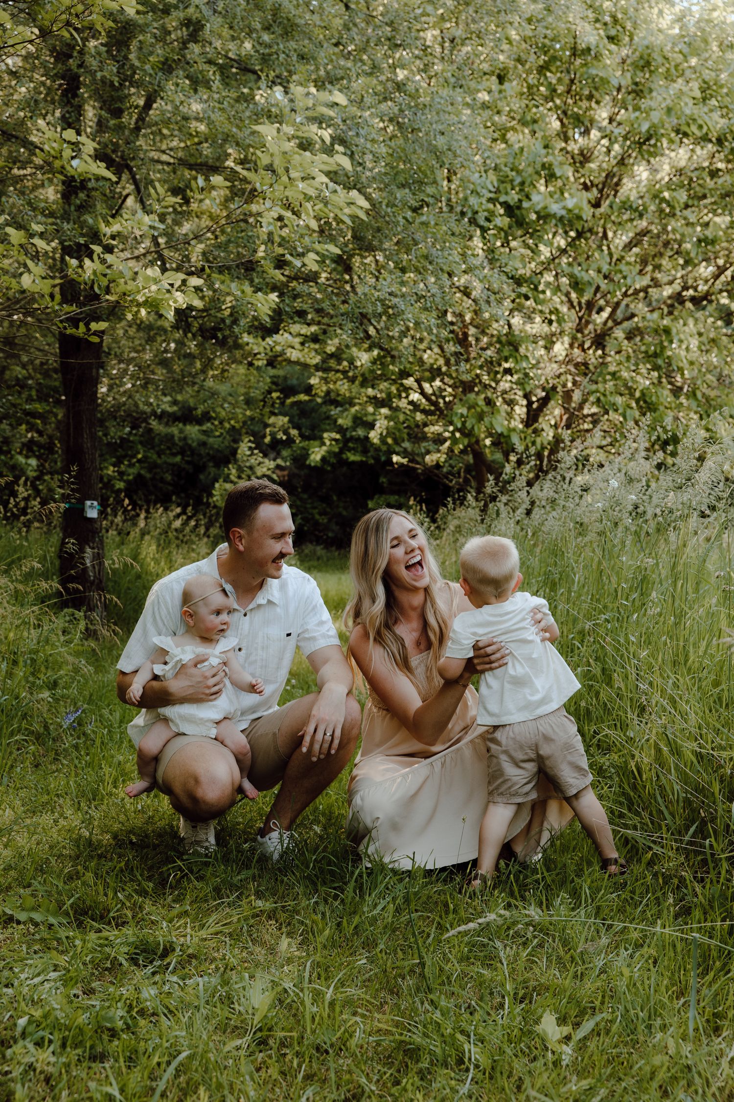 Family laughing together while sitting in tall grass during an outdoor photoshoot.