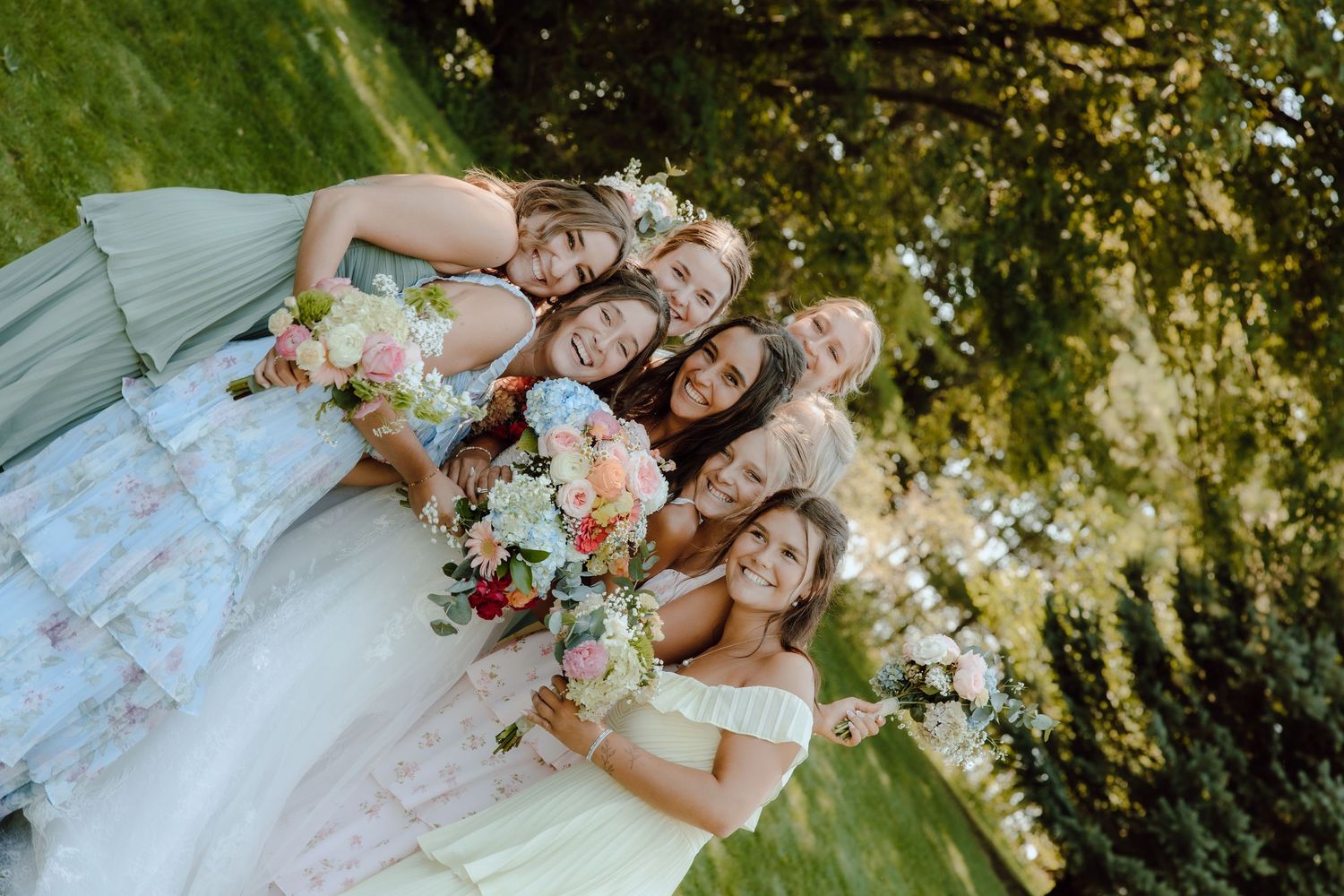 Bride and bridesmaids posing together outdoors holding colorful floral bouquets in elegant dresses.