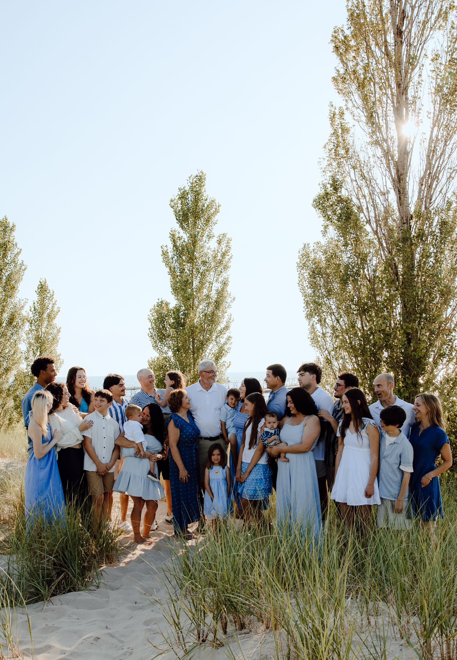 Wedding party in coordinated blue and white attire gathers on sandy dunes.