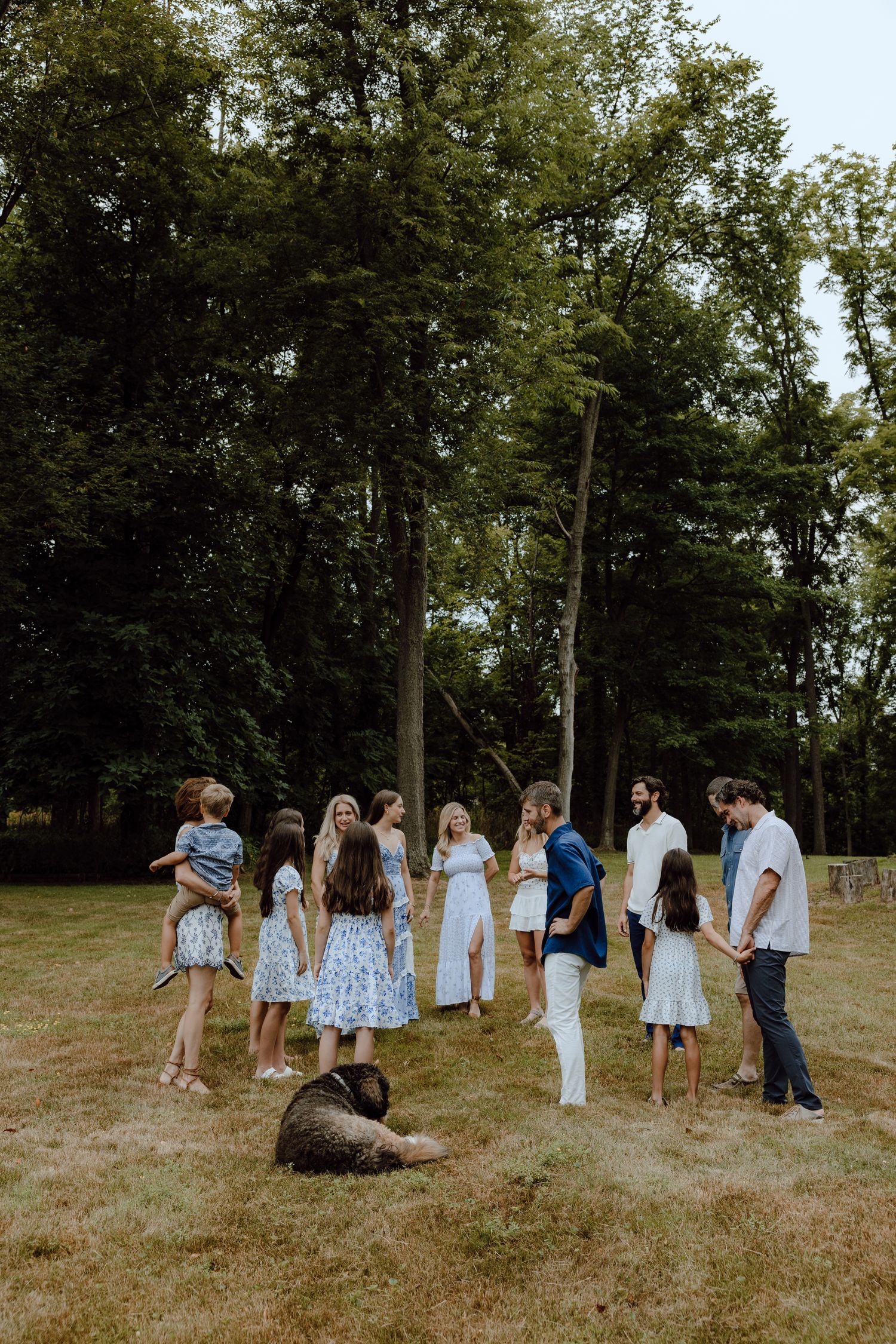 A casual gathering of people in coordinated outfits standing in a wooded area with a dog.