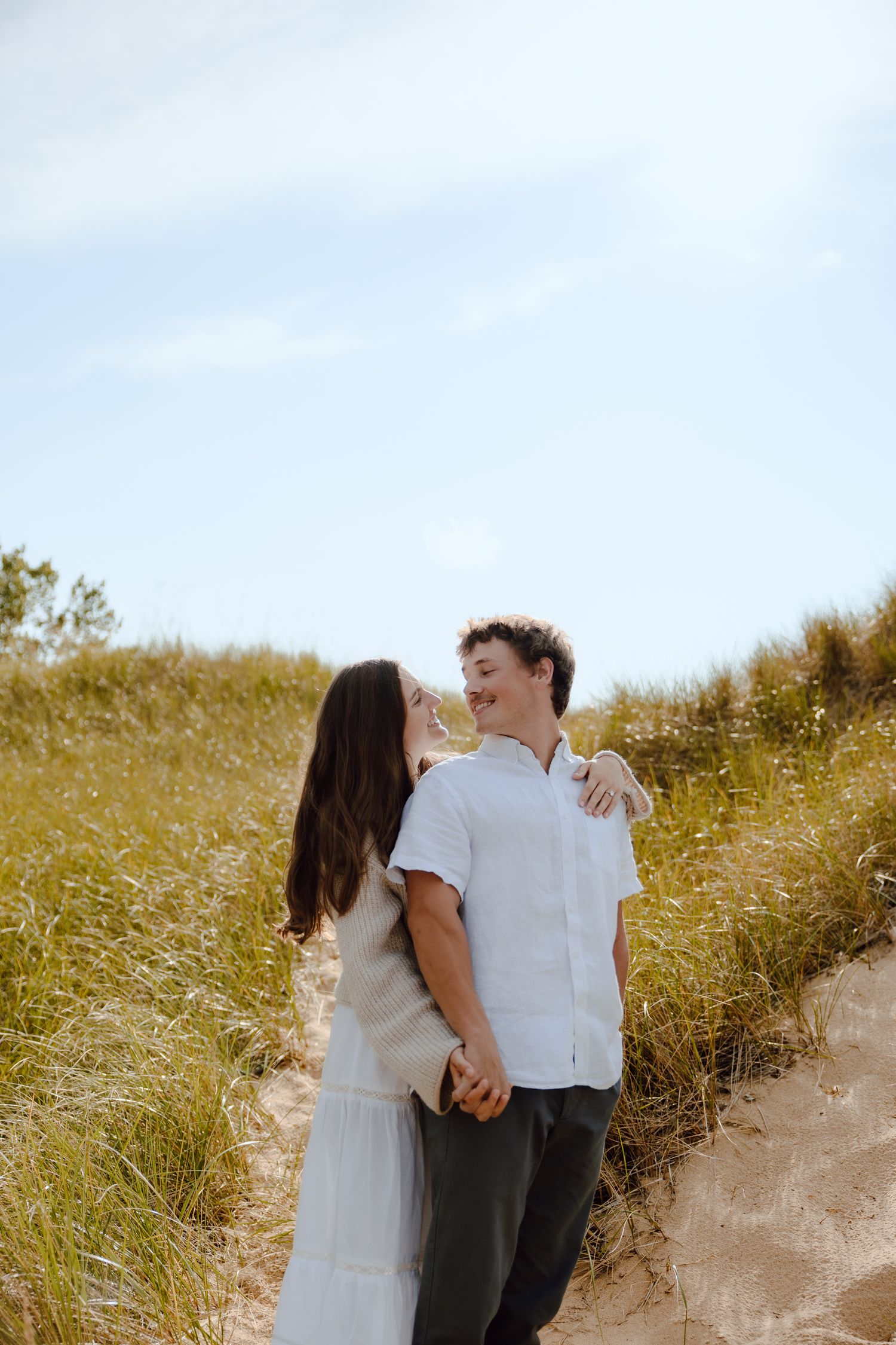 Couple in light colored clothing sharing tender moment on grassy hillside.