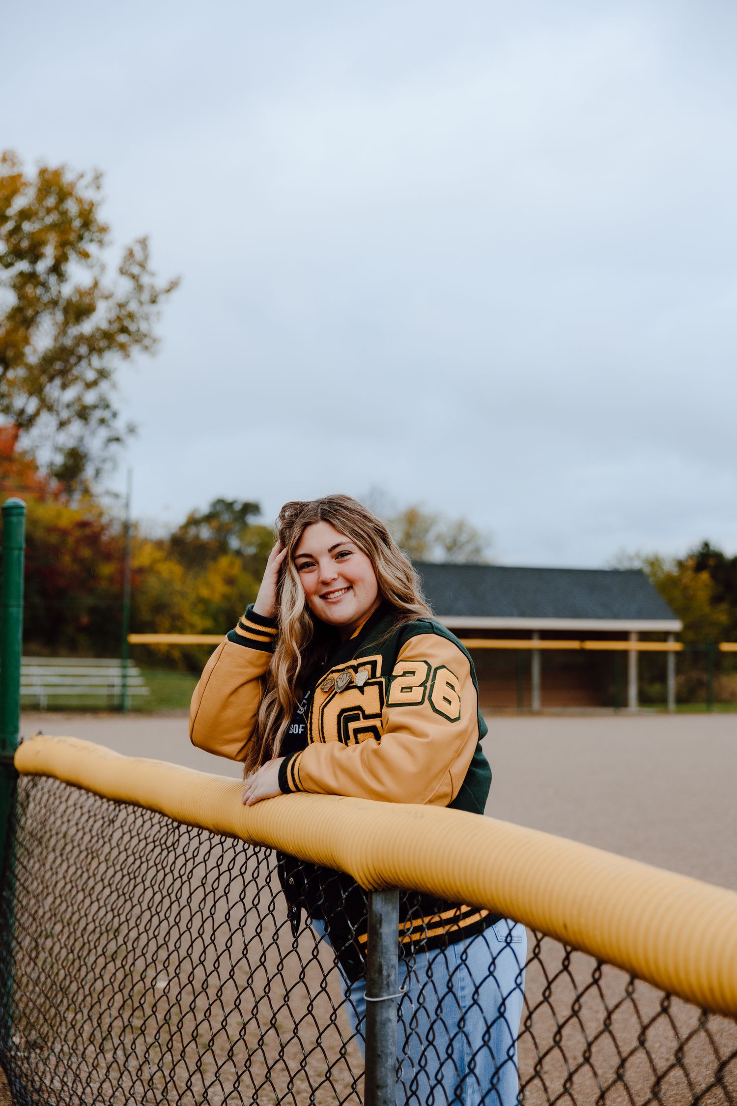 Outdoor portrait session leaning on a chain link fence at a sports field.