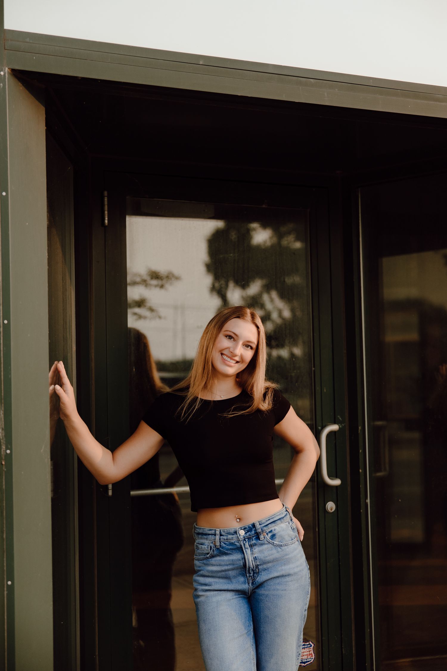 Woman in casual attire posing against a modern building exterior with dark doors.