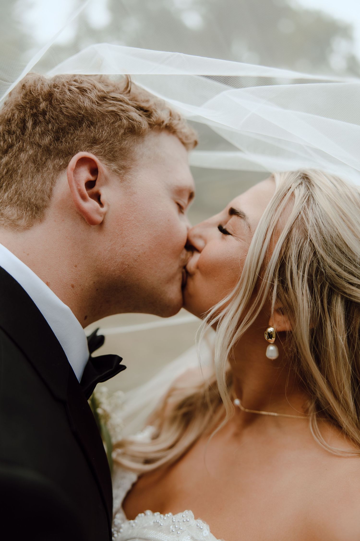 Bride and groom sharing a romantic kiss under a flowing white wedding veil.