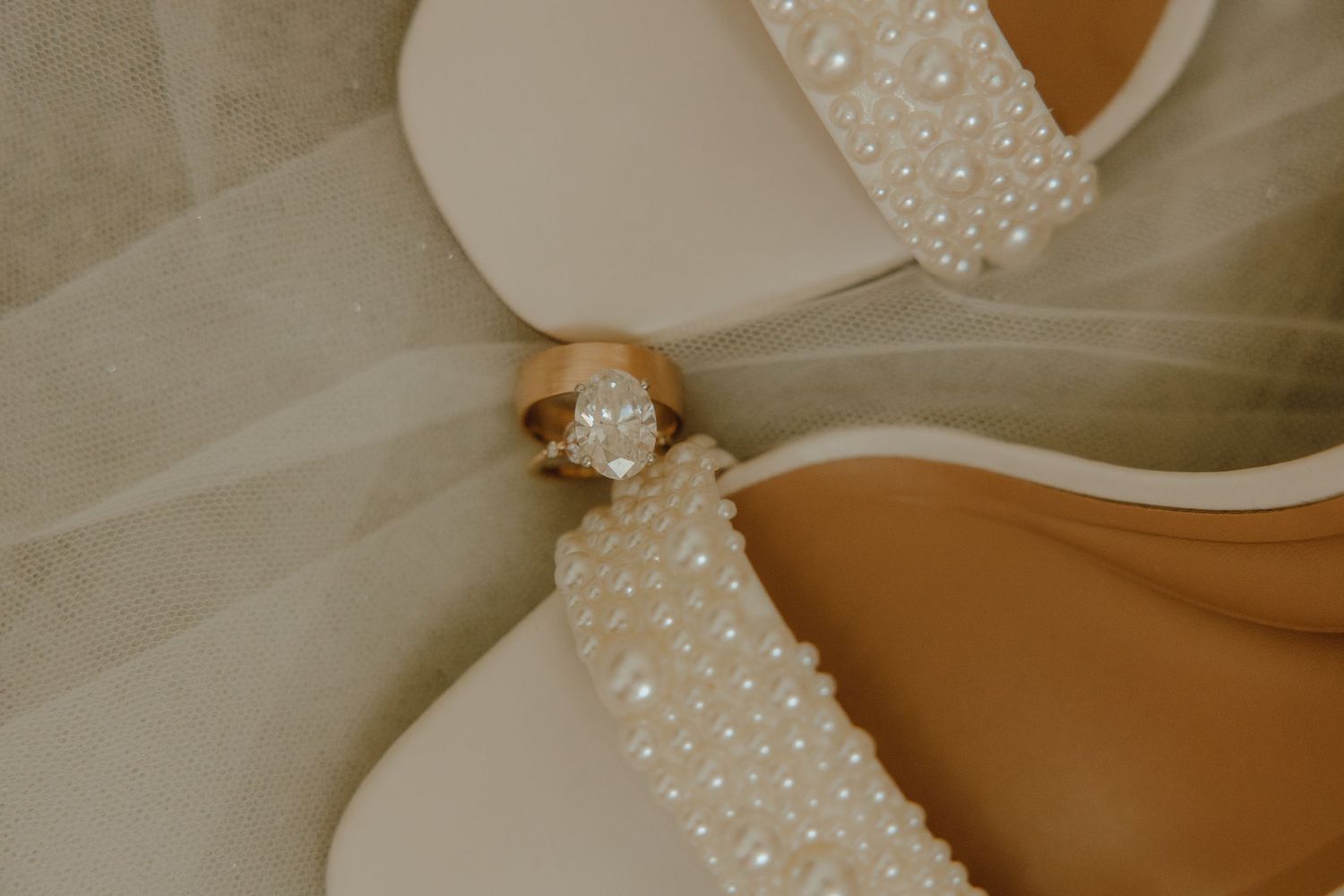 Pearl-embellished white wedding shoes with gold diamond engagement ring and wedding band displayed elegantly.