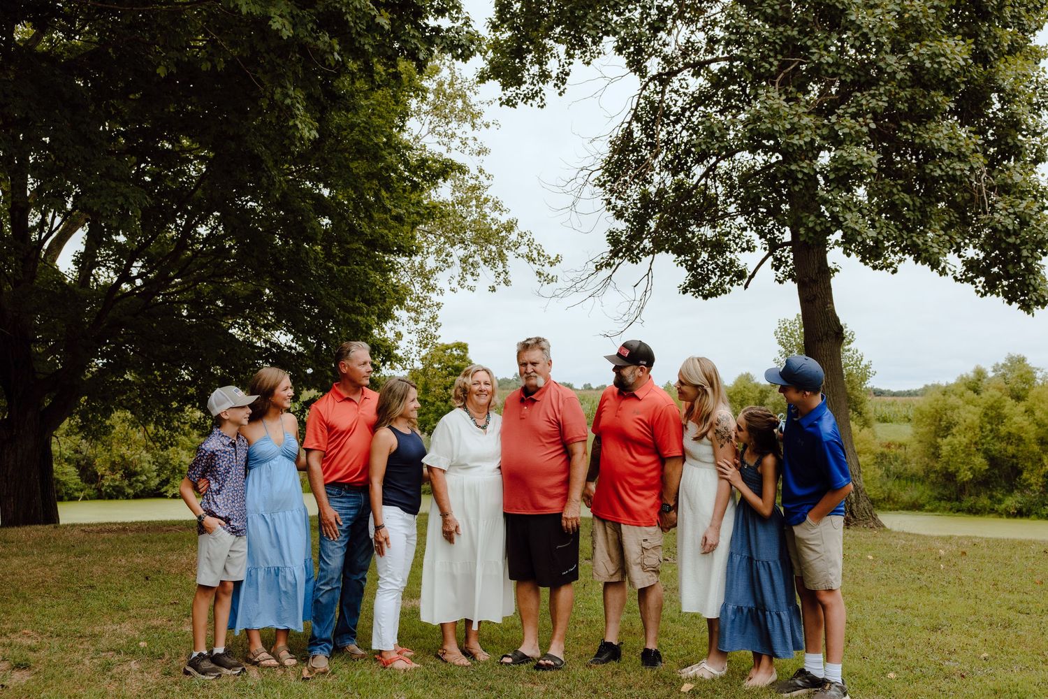 Large family group poses together outdoors on a sunny day wearing casual clothing.