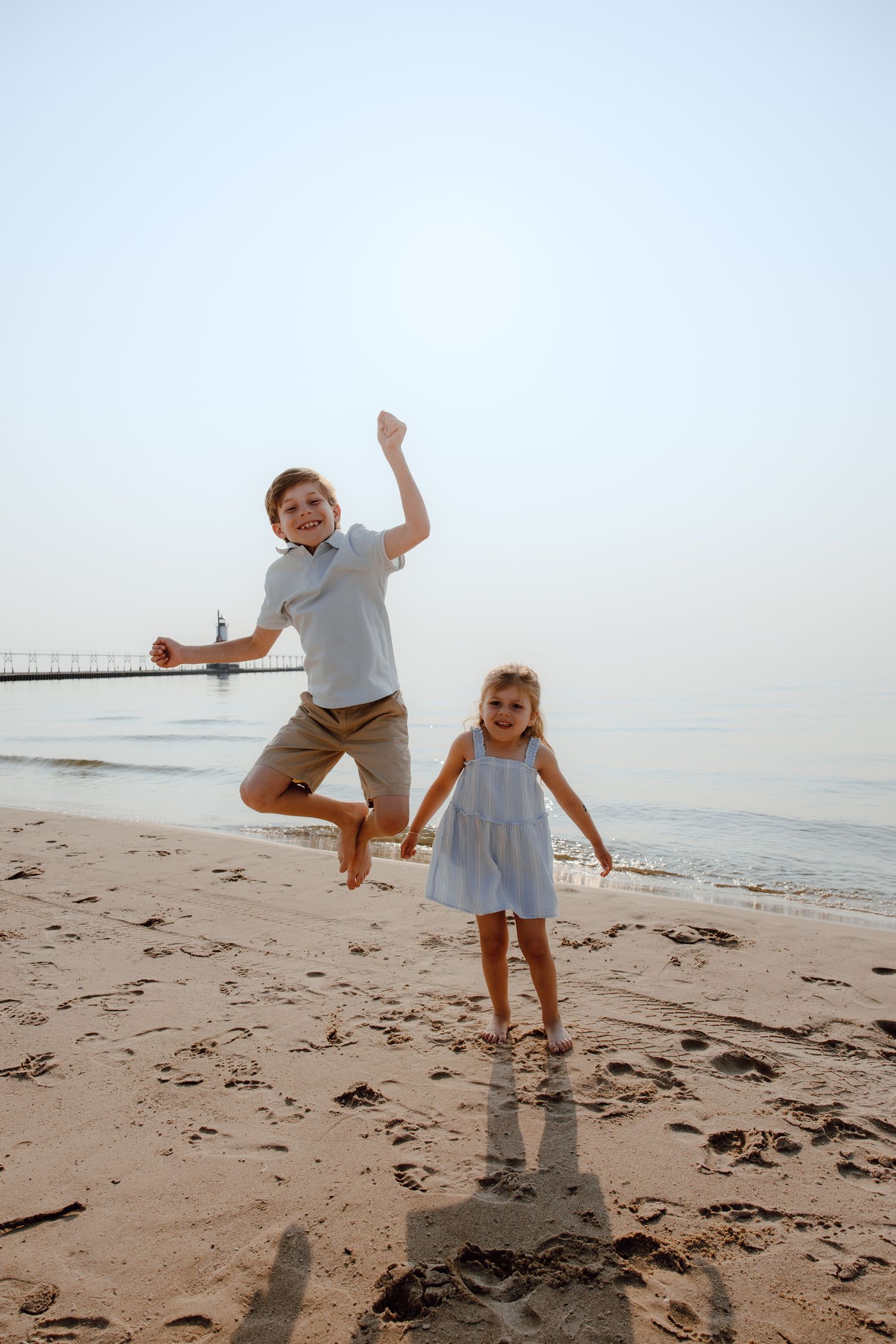 Two children jumping and playing on a sandy beach at sunset.