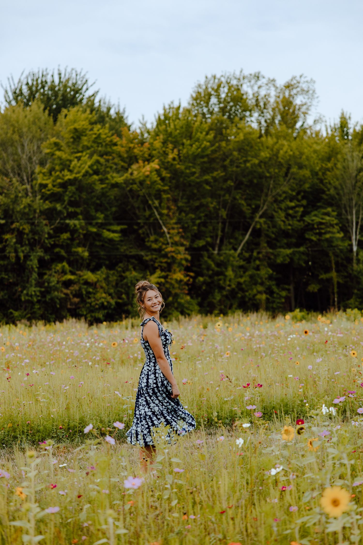 A person in a blue and white patterned dress twirls through a wildflower meadow on a sunny summer day.