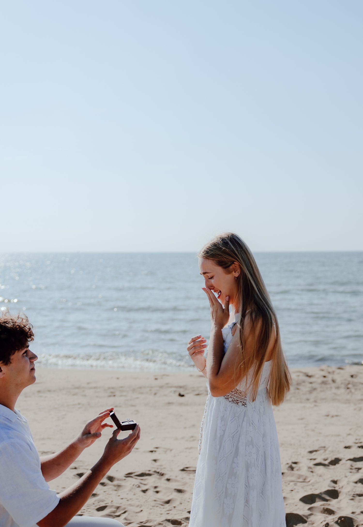 Surprise beach proposal moment captured in bright daylight by the ocean.