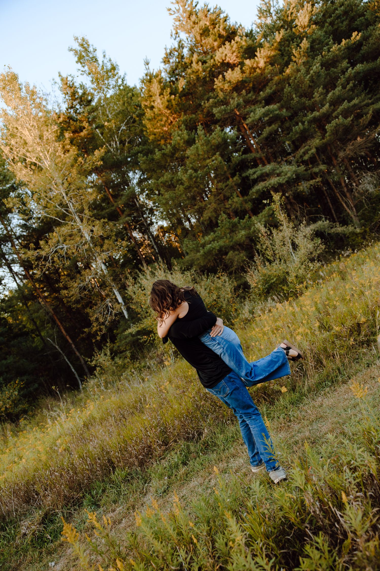 A playful moment captured on a hillside with pine trees in the background.