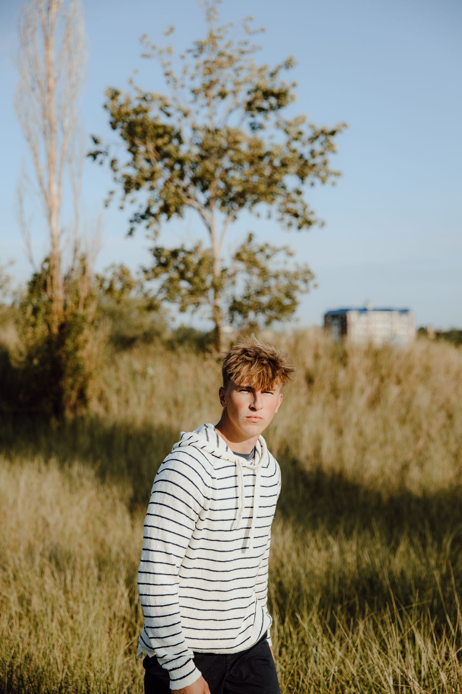 Person wearing striped hoodie sitting in tall grass during golden hour.