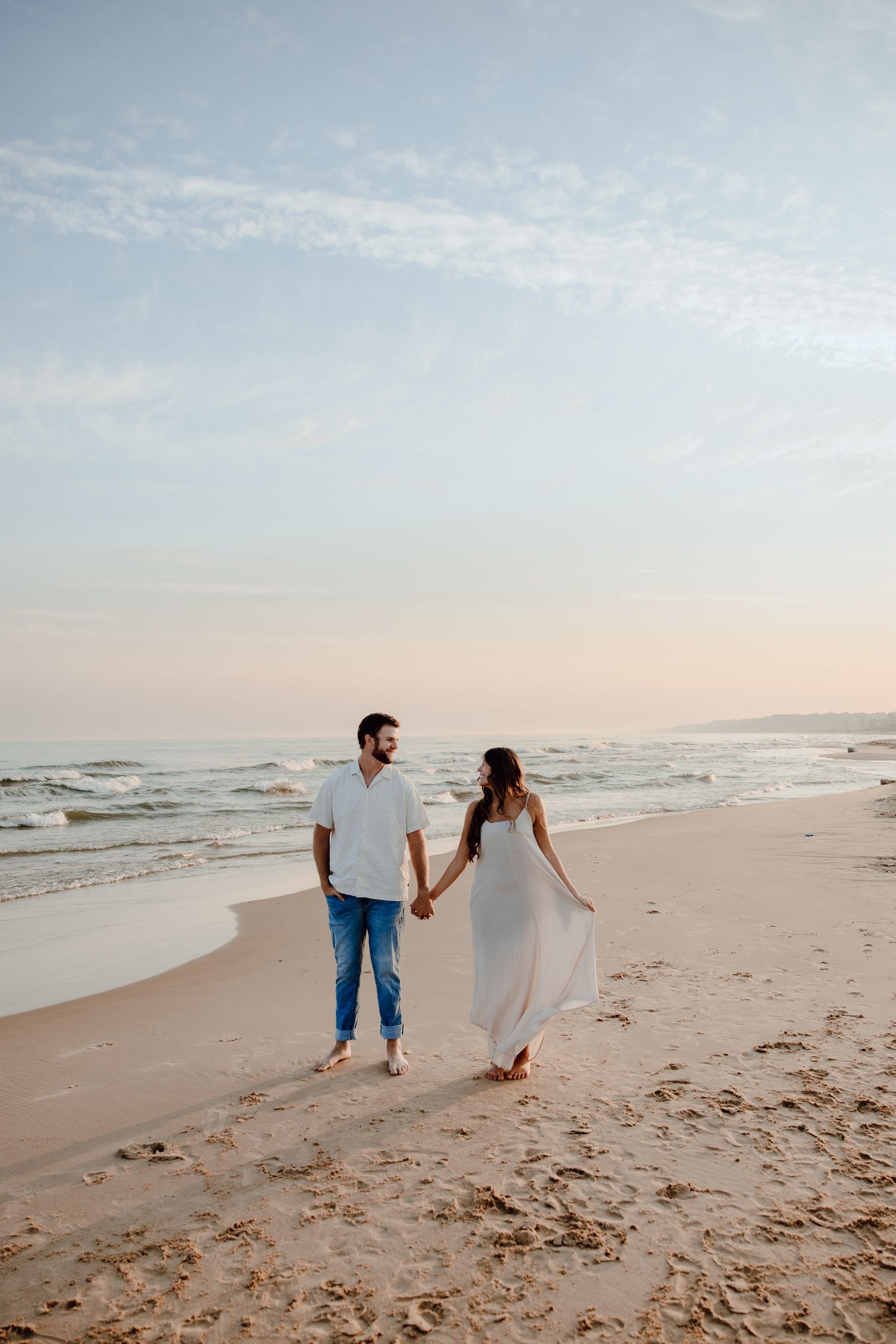 Couple holding hands while strolling along a scenic beach during sunset.
