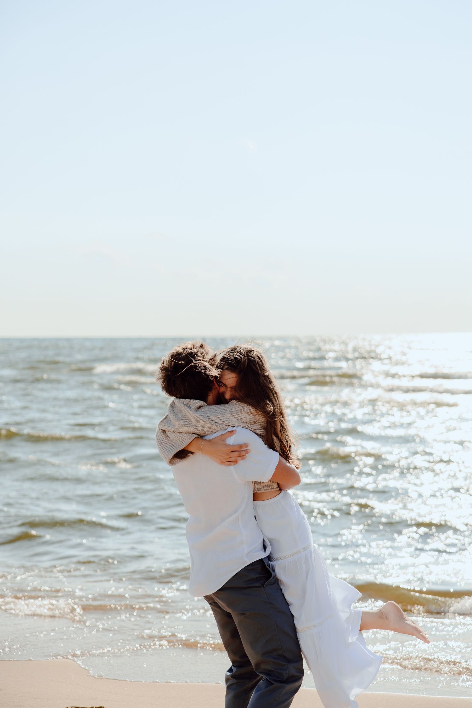 Couple in white clothing embracing and spinning on sunny beach.