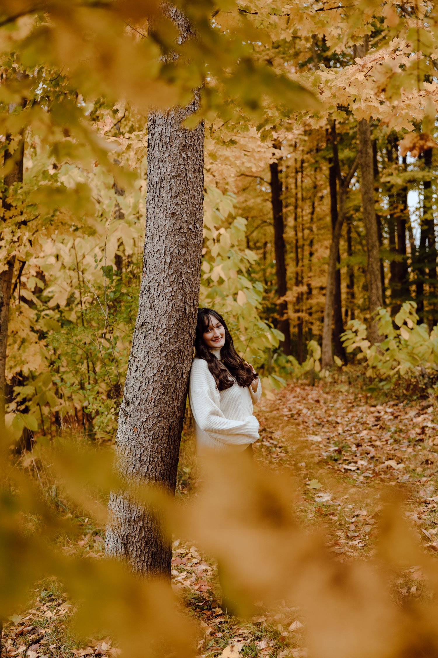 Artistic autumn portrait through blurred golden foliage in a wooded setting.