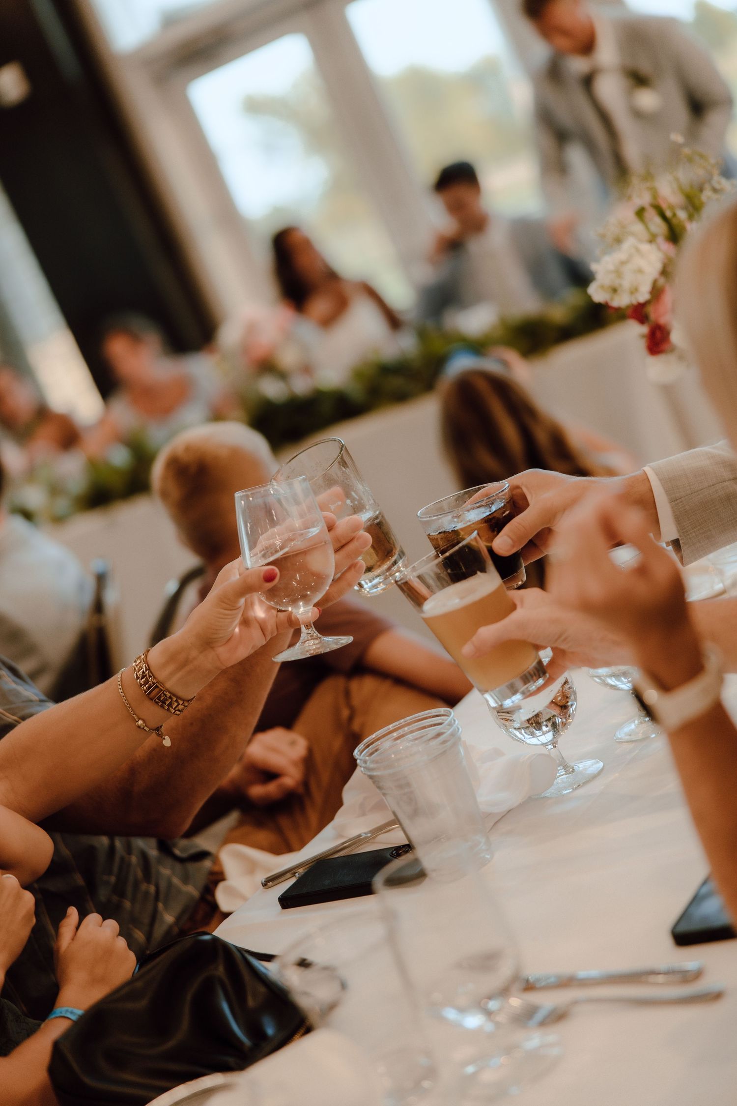 Wedding guests clinking wine glasses during a toast at an elegant indoor reception with floral decorations.