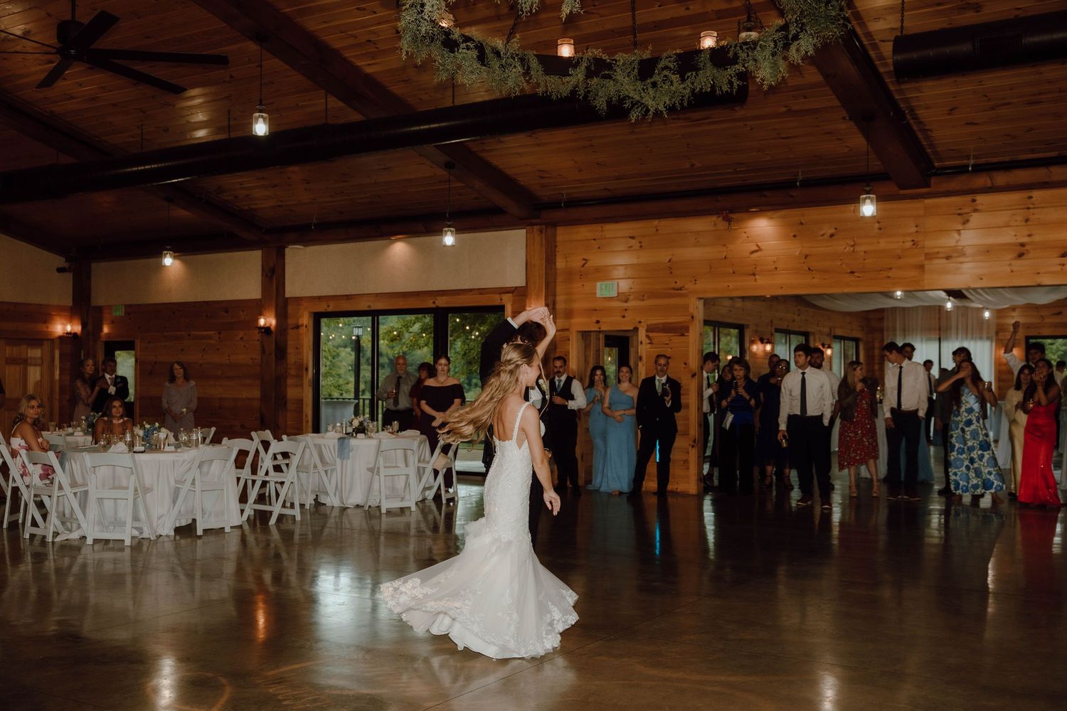Bride and groom share first dance in rustic wood-beamed wedding reception venue.