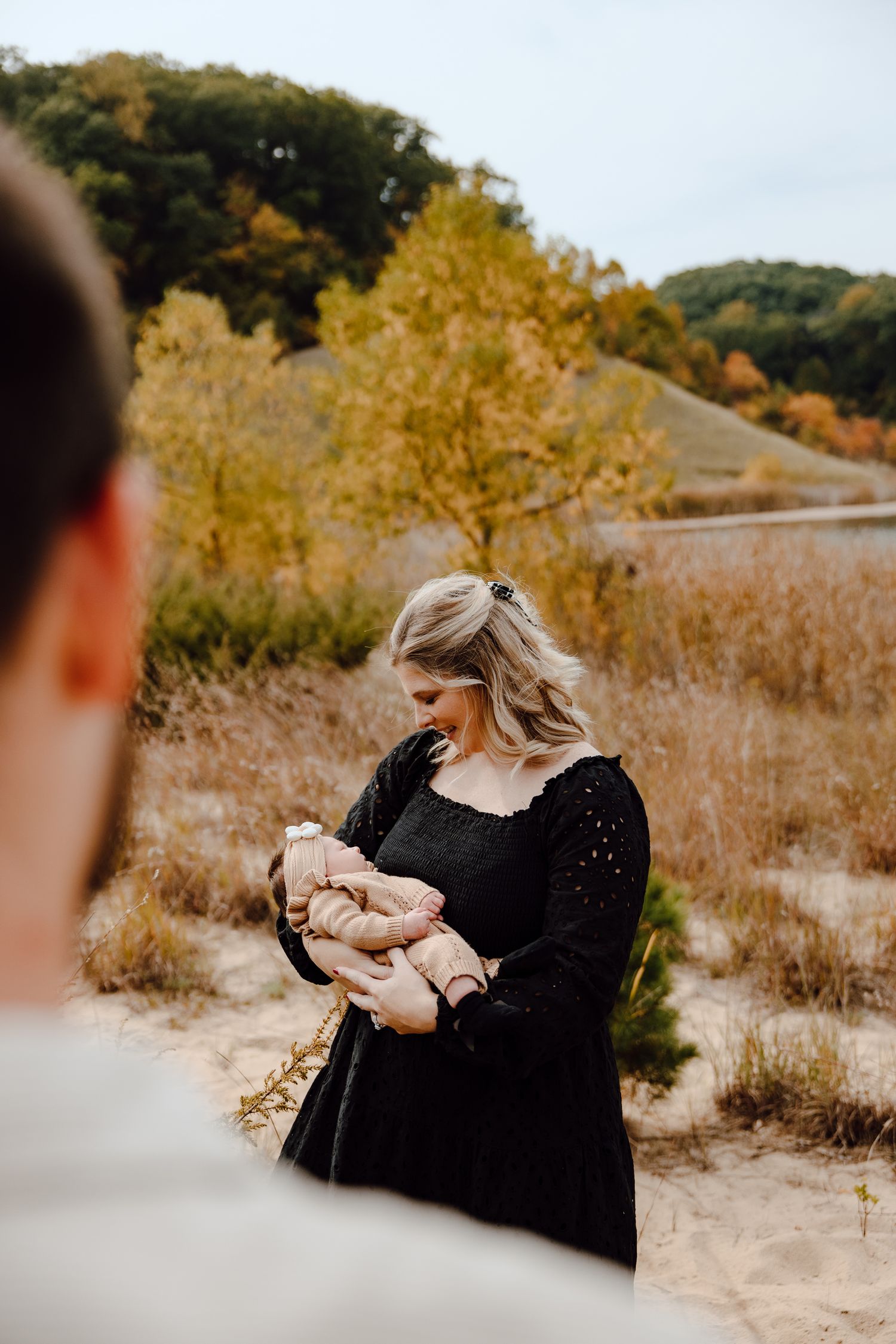 A couple embraces in a golden autumn field during sunset with trees in the background.