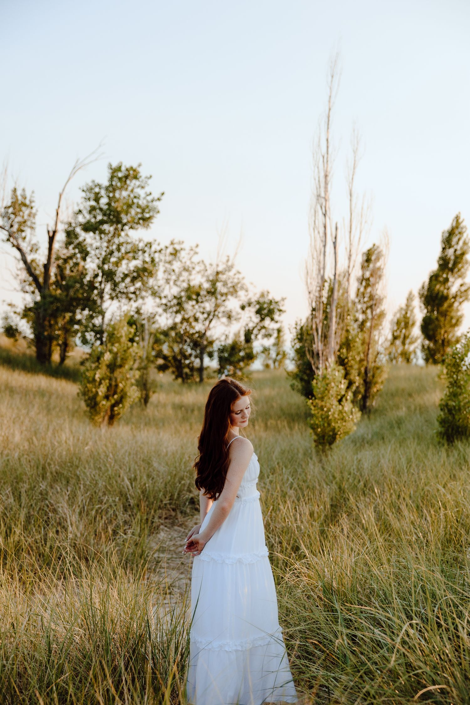 Someone in a flowing white dress walks through tall grass at sunset.