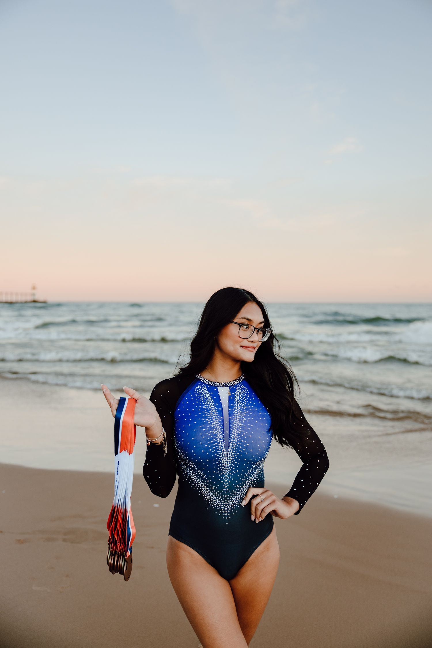 A sparkly blue and black leotard catches the light during a beachside photoshoot at sunset.