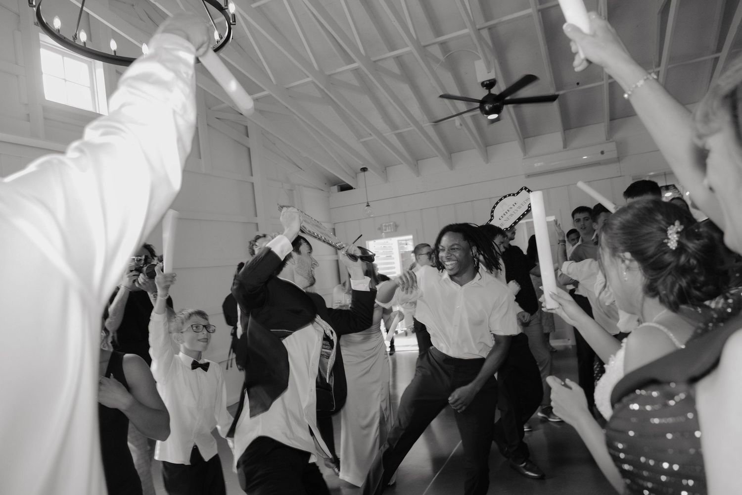 Black and white photo of wedding guests dancing and celebrating energetically on the dance floor at a reception.