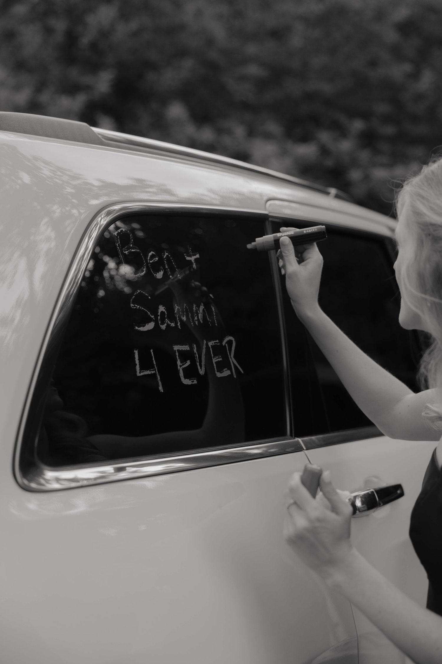 Guest writes Ben and Sammi 4 Ever on a classic white wedding car window in black and white photo.