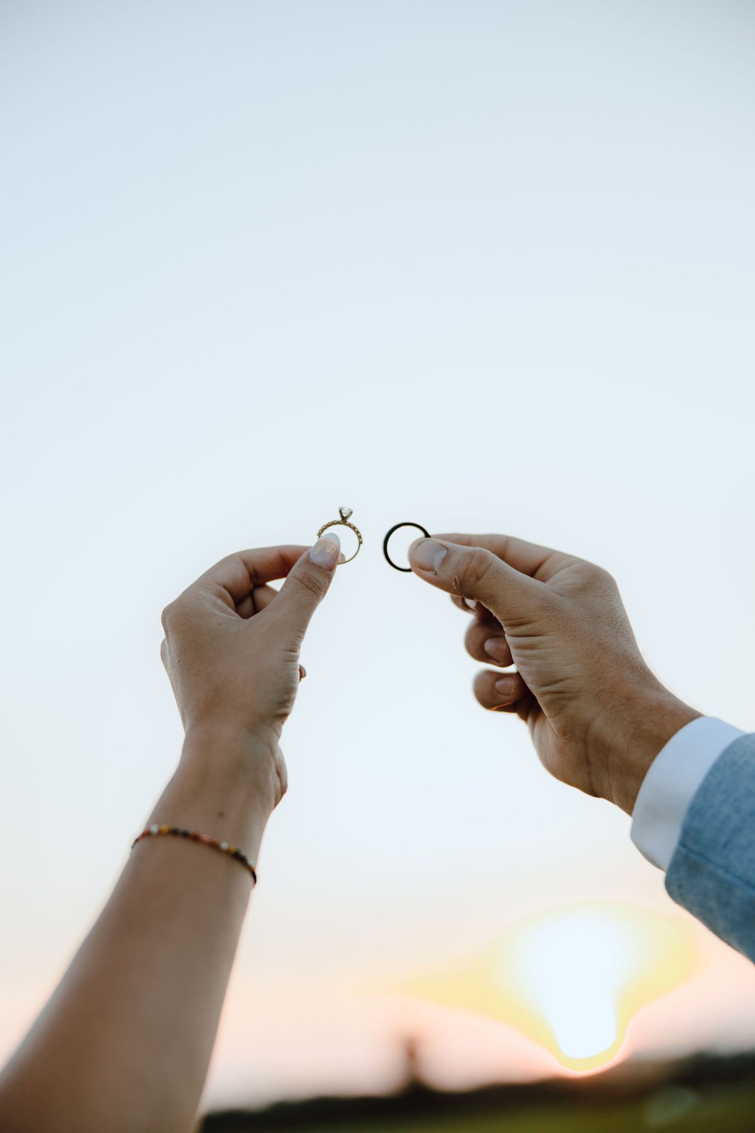 Couple holding wedding rings up against a sunset sky, symbolizing their marriage commitment.