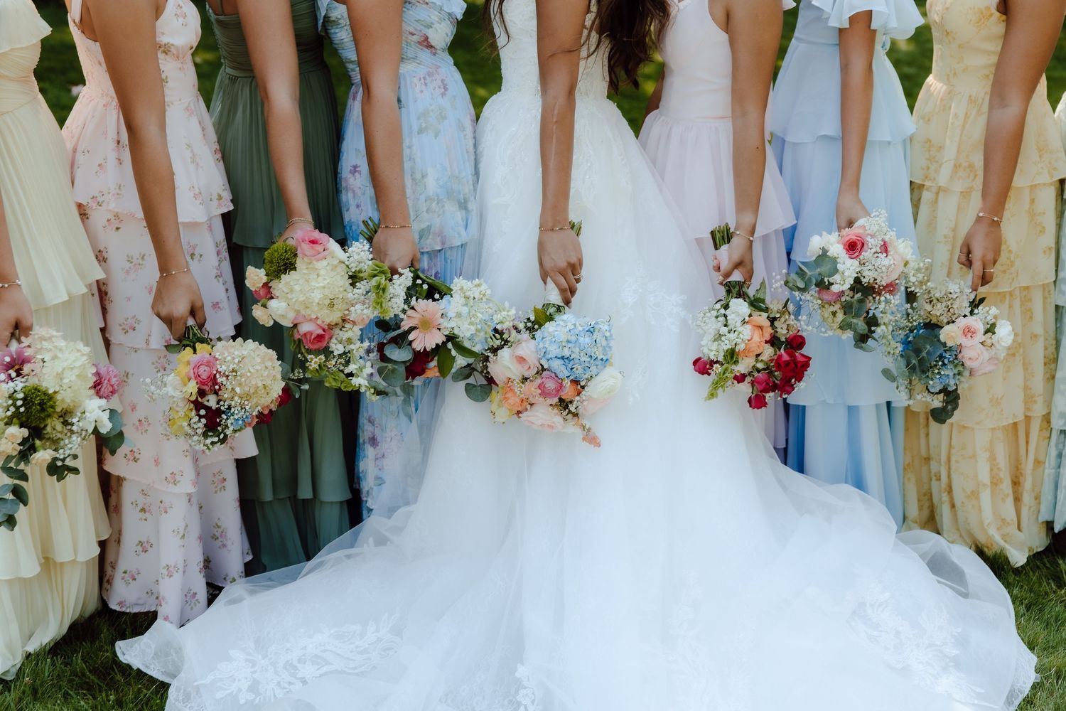 Bride and bridesmaids in colorful mismatched dresses holding vibrant floral bouquets at an outdoor wedding.