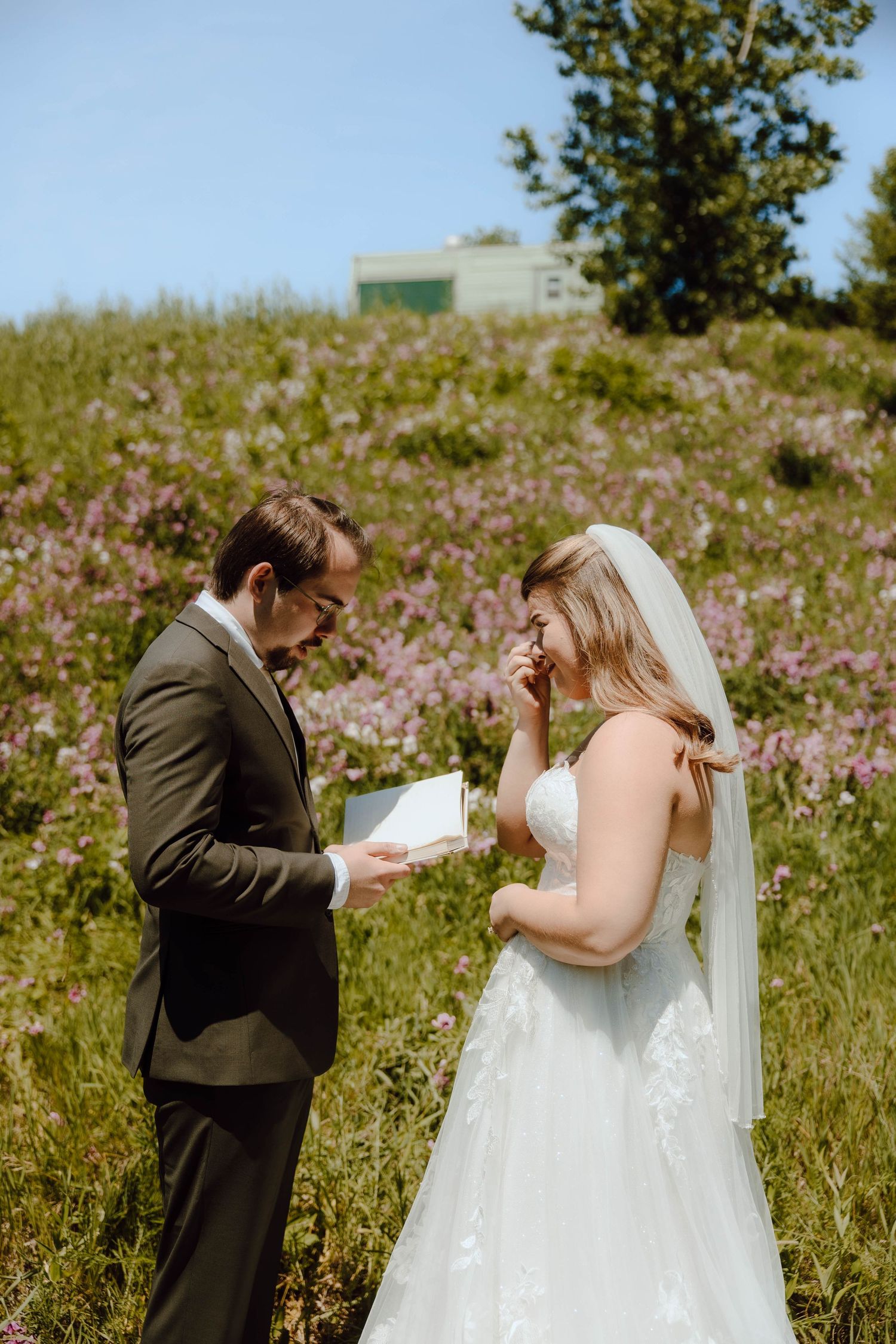 Groom reads heartfelt vows to emotional bride in a wildflower meadow on their wedding day.