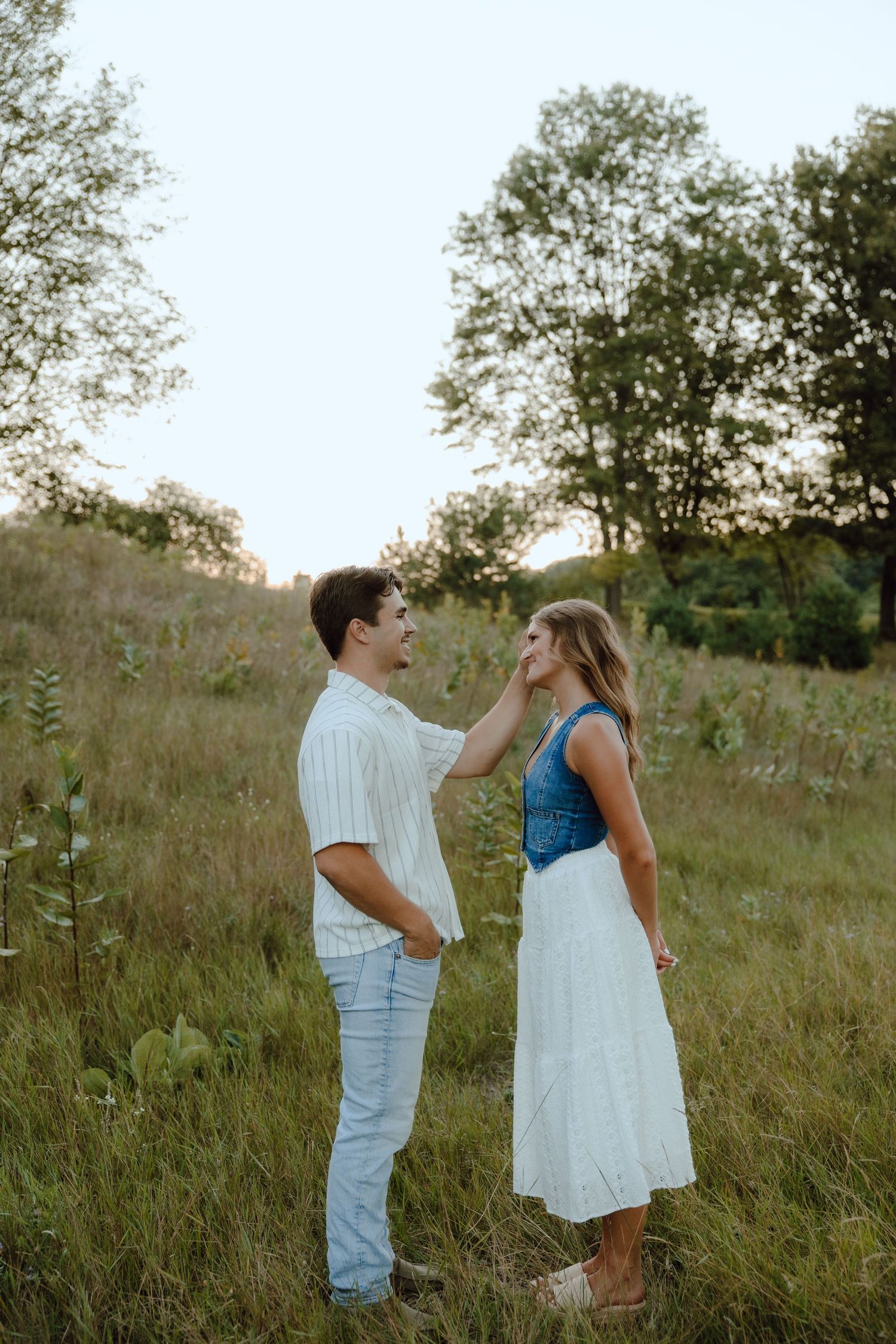 Couple sharing a tender moment in a lush green meadow, man gently touching woman's face at sunset.