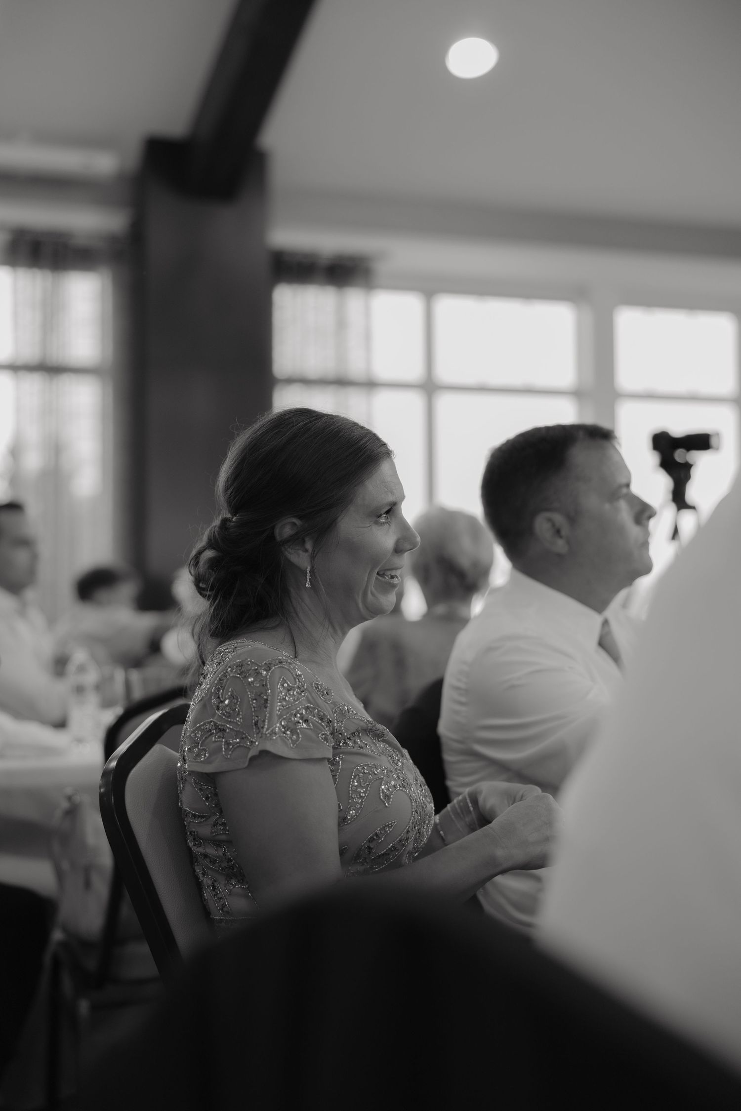A woman in a sequined dress laughs joyfully during a wedding reception in a elegant banquet hall.