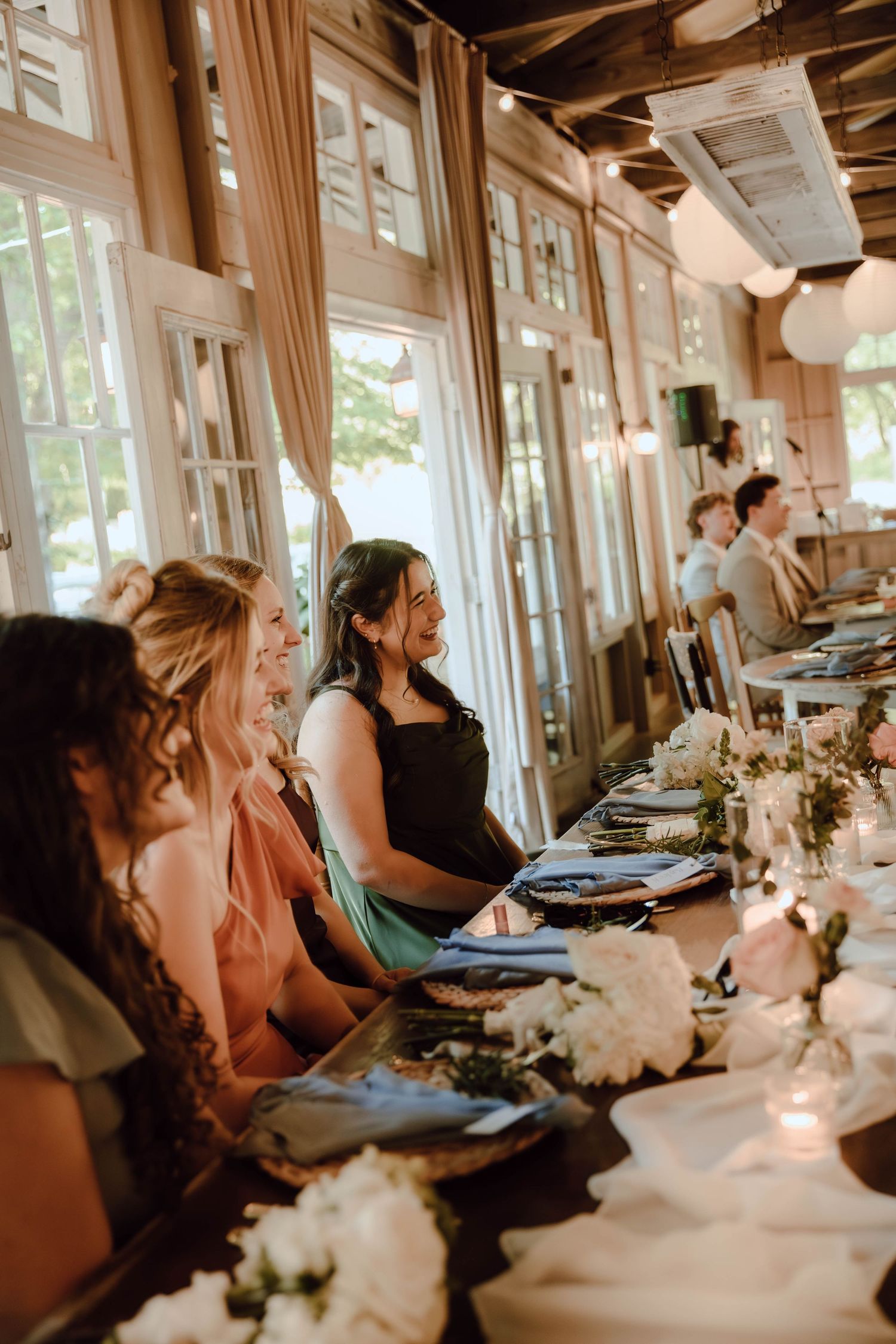 Wedding guests seated at elegantly decorated reception table with white floral centerpieces in a warmly lit venue.