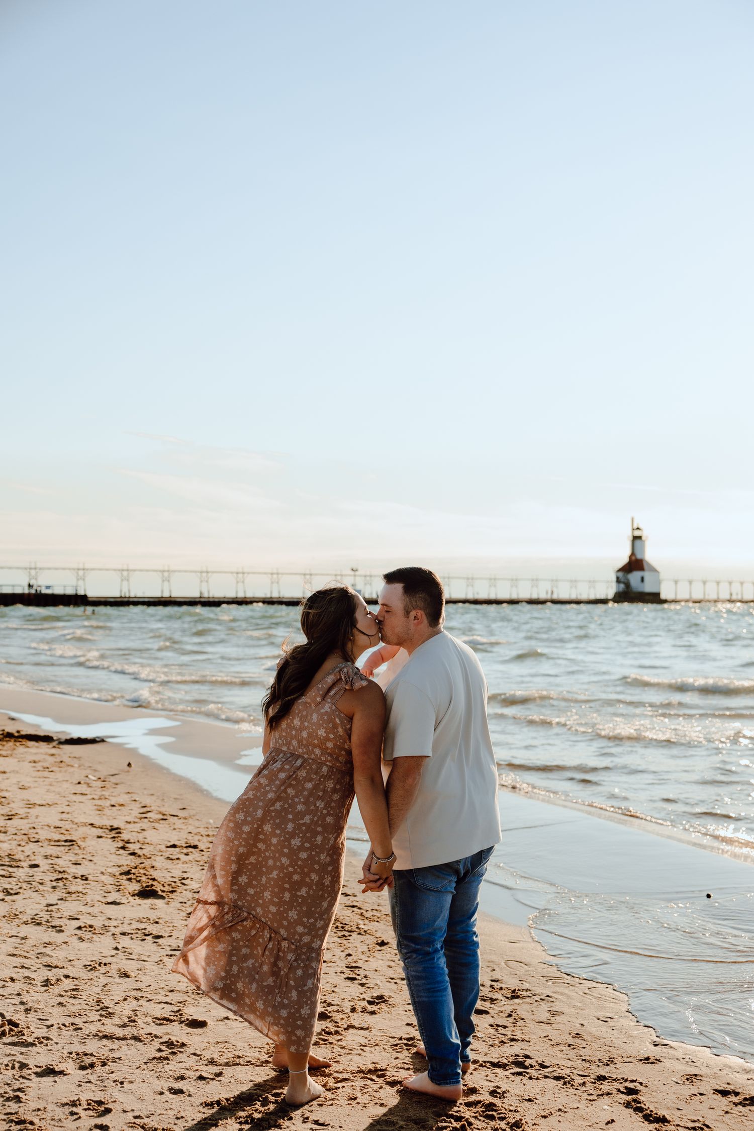 Couple walking along beach with lighthouse visible in background.