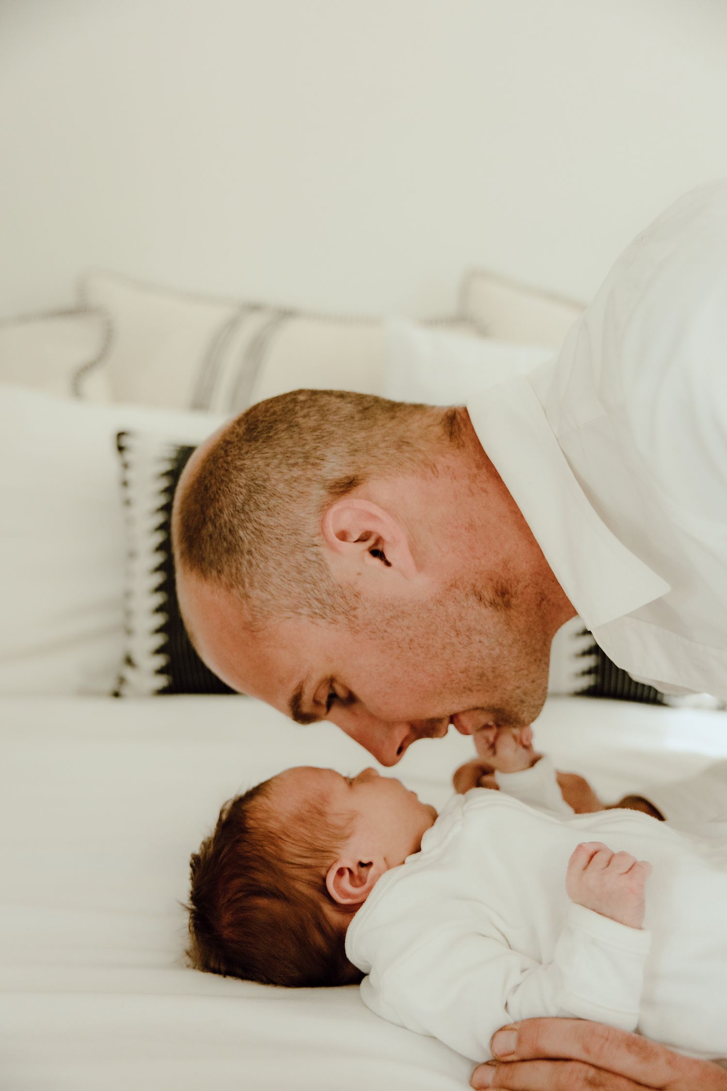 An intimate moment between parent and baby lying together on white bedding.