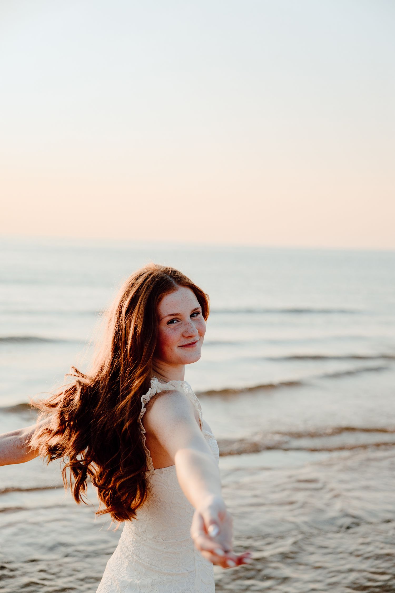 Someone in white spins on the beach at sunset with hair flowing in the wind.