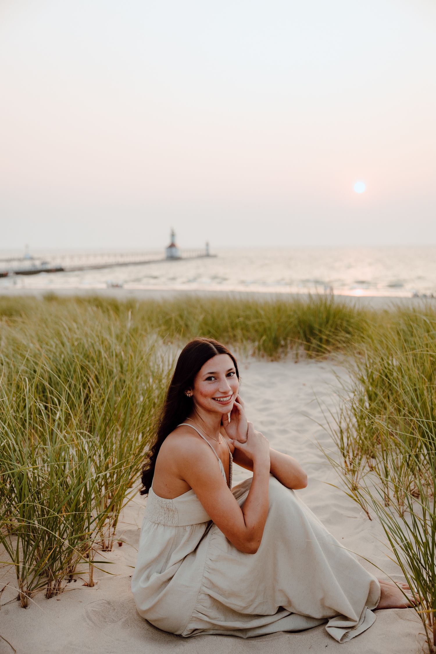 Sunset beach portrait with woman in white dress reclining among dune grass.