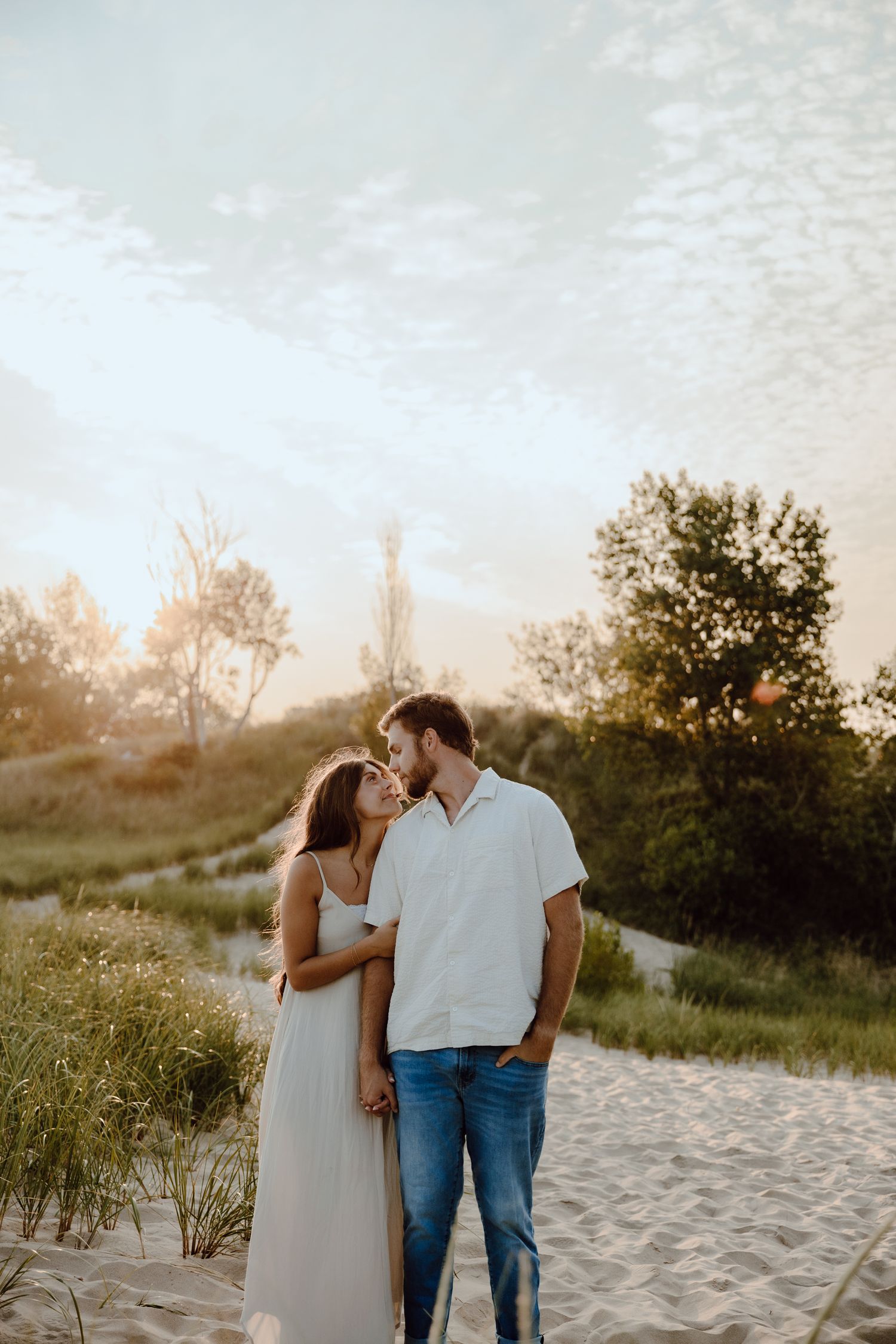 A romantic couple embraces on a sandy beach path during golden hour.