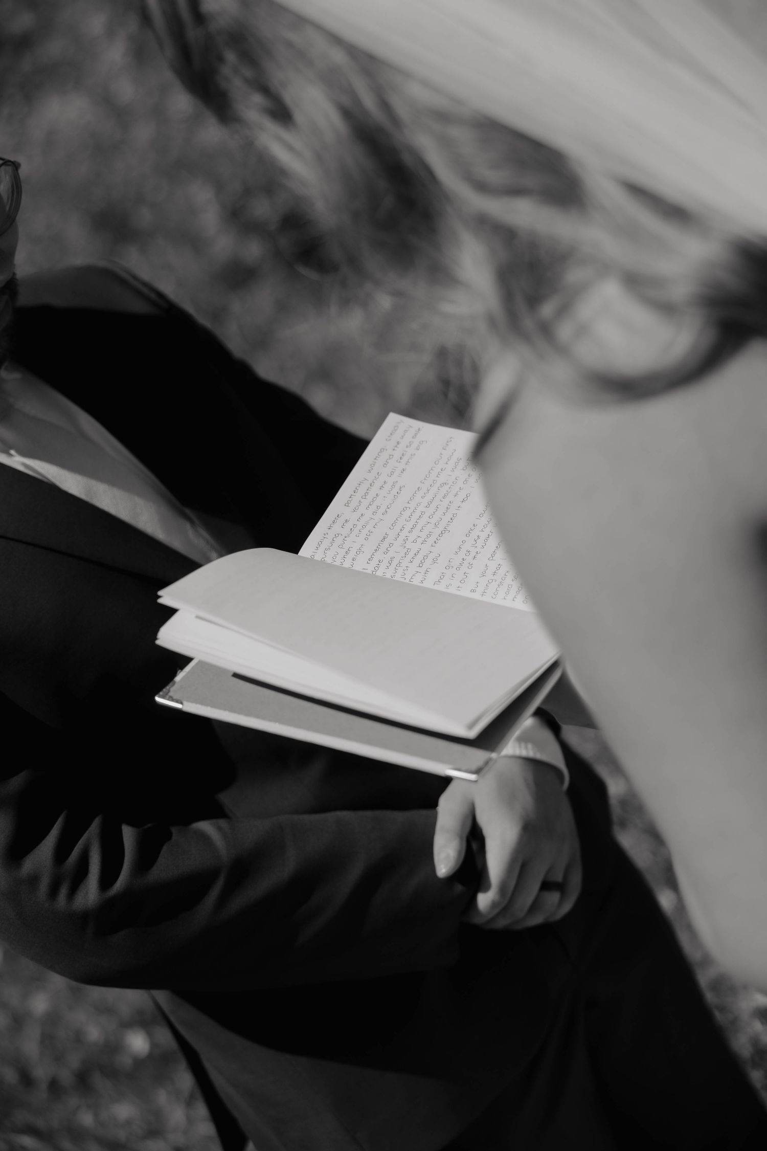 Black and white photo of groom reading handwritten wedding vows from small notebook.