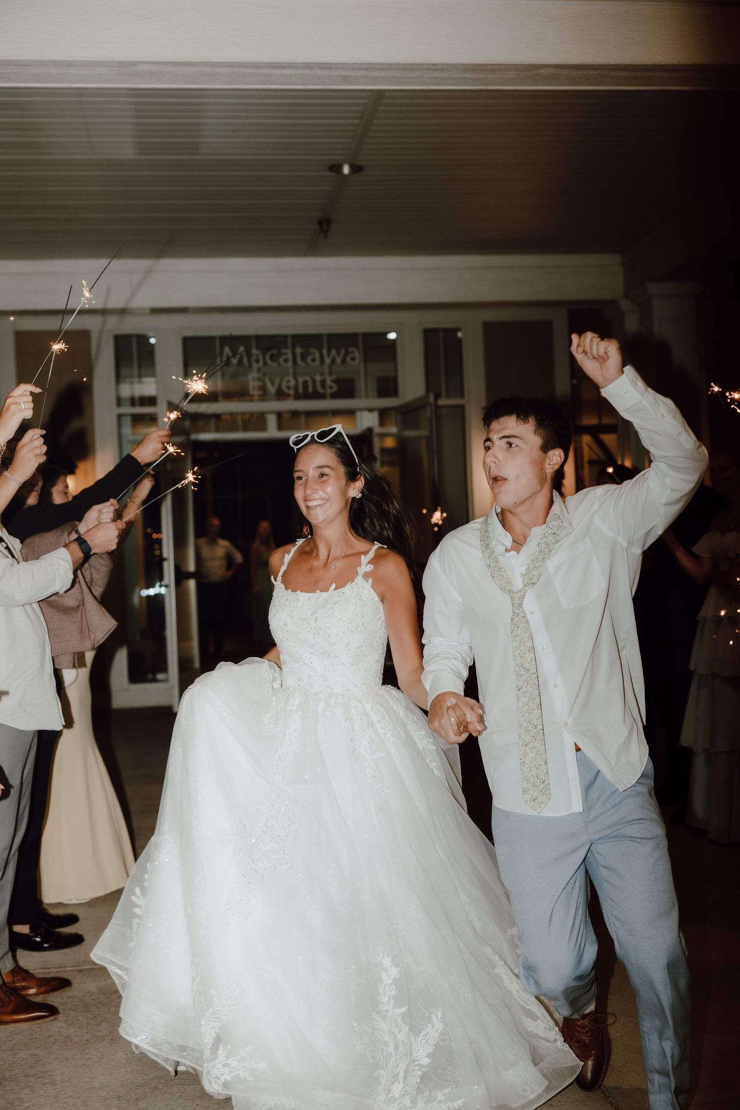 Bride and groom exit wedding venue through sparkler sendoff celebration at night.