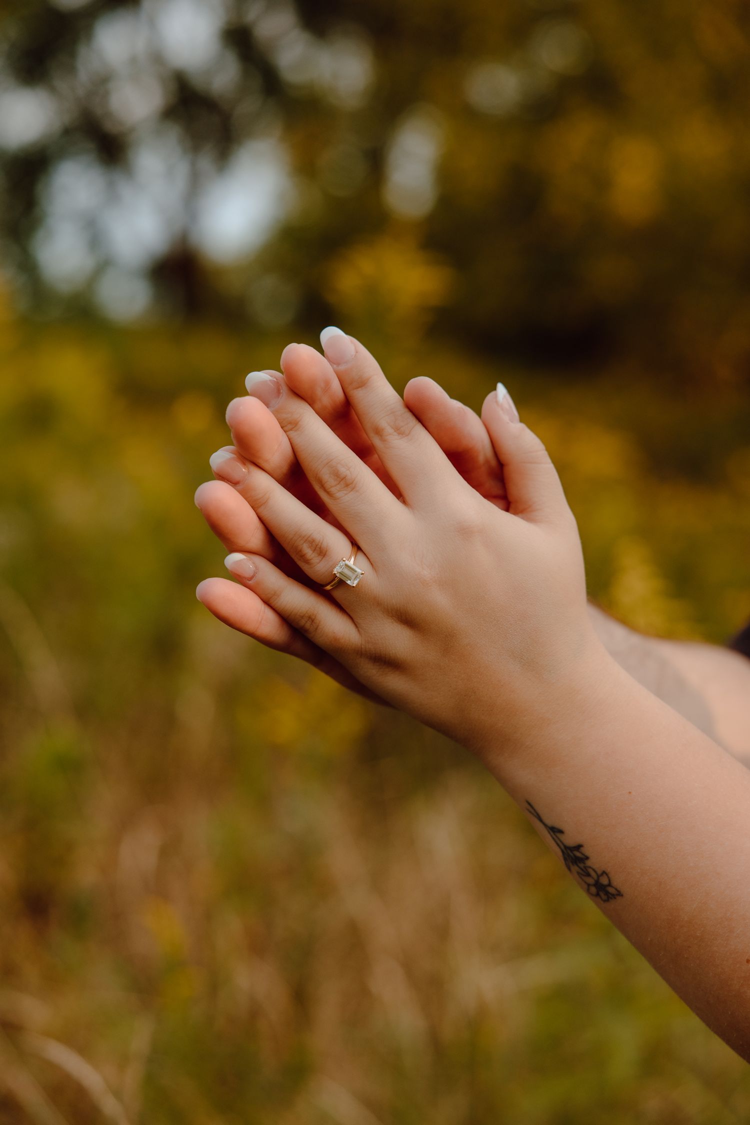 Close-up of hands displaying an engagement ring against an autumn background.