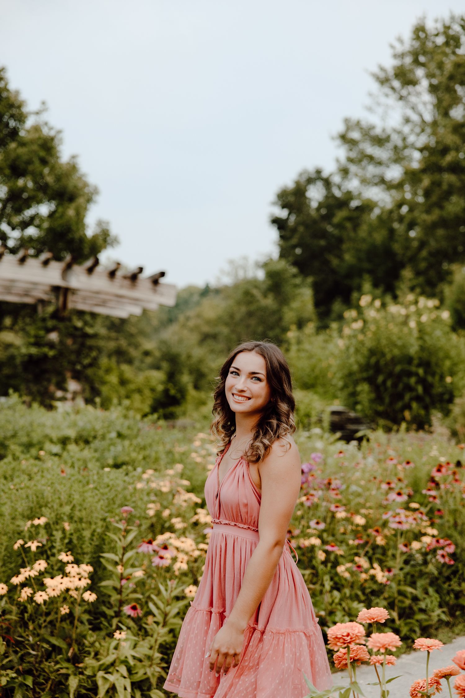 Summer garden portrait with pink dress surrounded by colorful flowers.