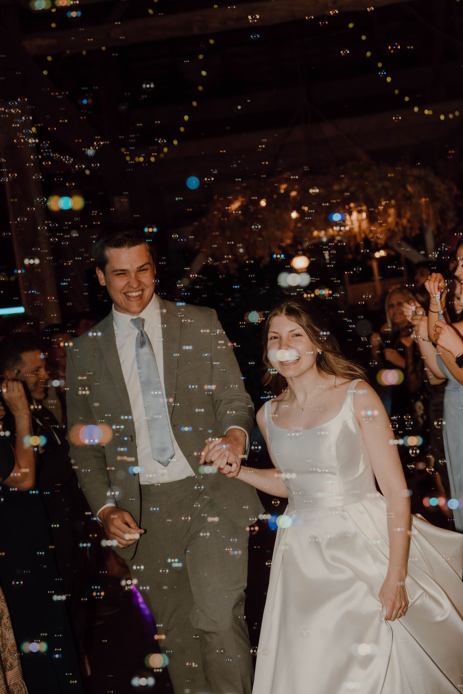 Happy bride and groom walking through bubbles during their wedding reception dance floor celebration at night.