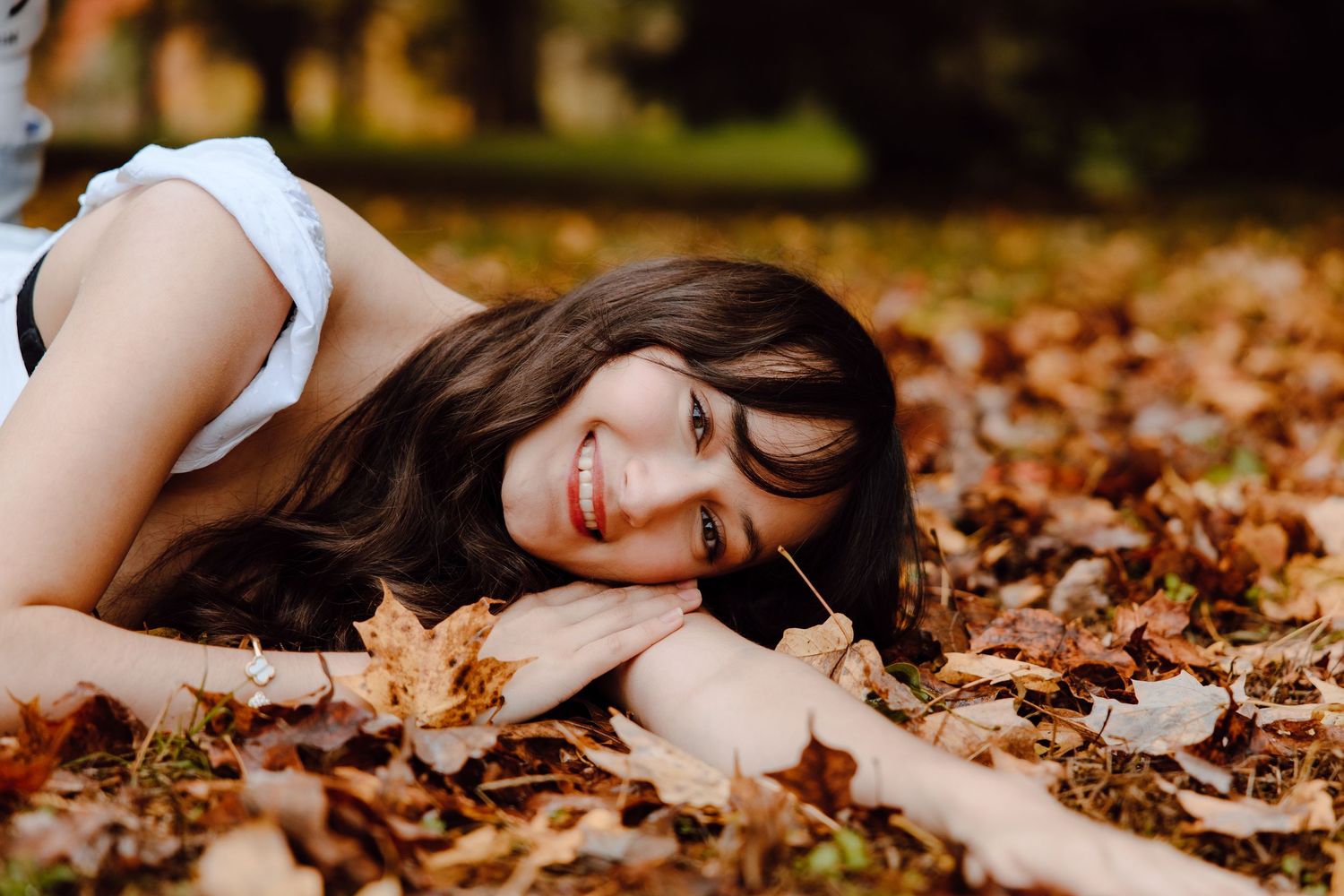 Artistic portrait lying in fallen autumn leaves during an outdoor photo session.