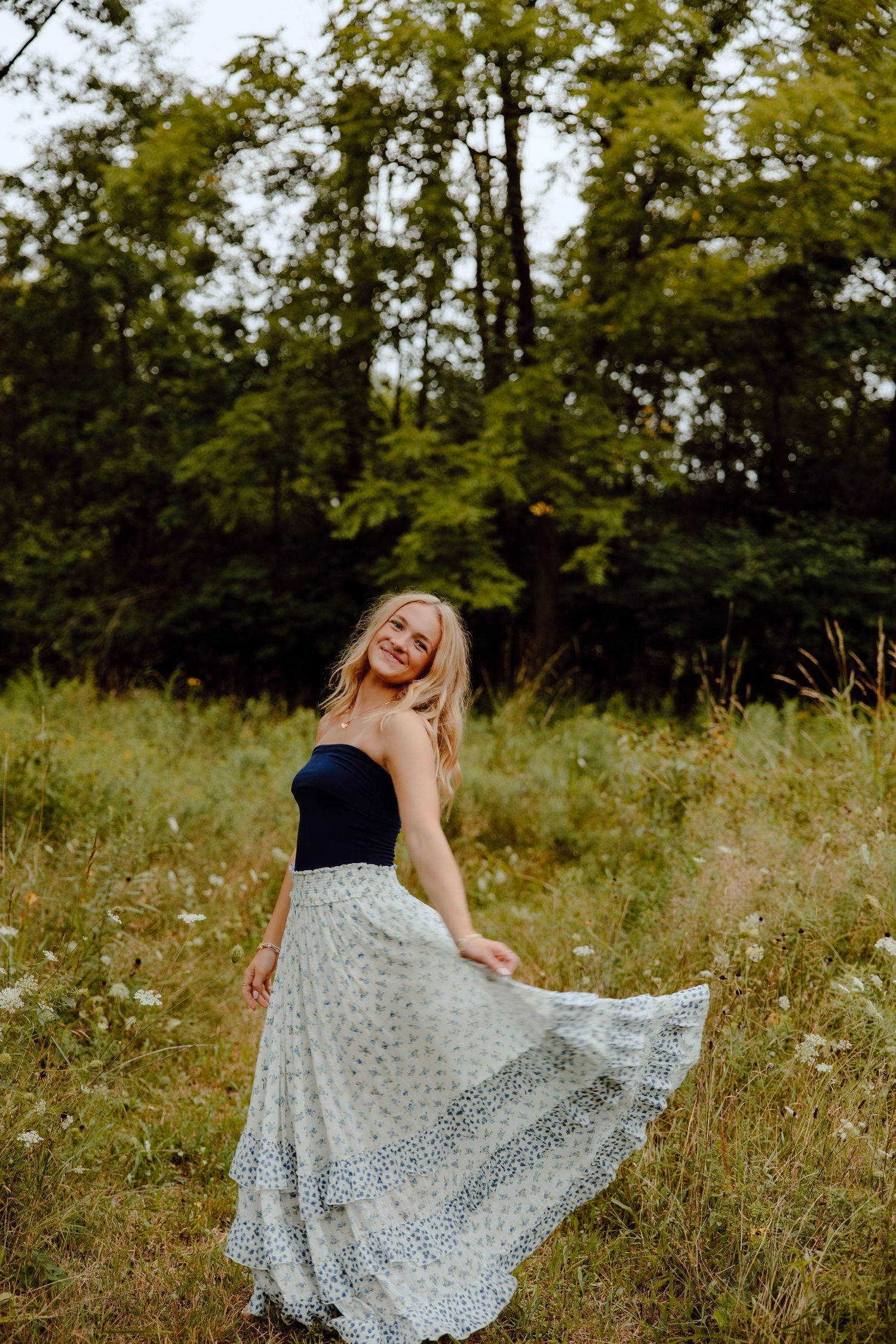 Person in black top and patterned skirt dances gracefully in a wildflower field.