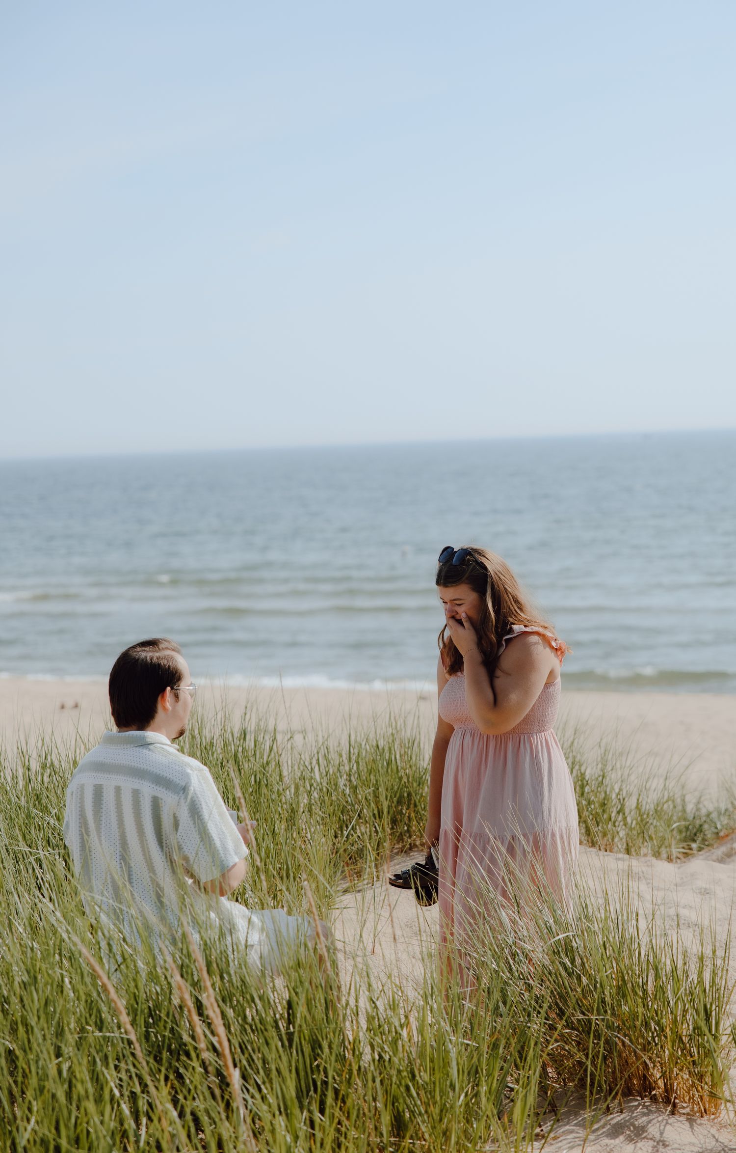 A couple walking through coastal dune grass by the ocean.