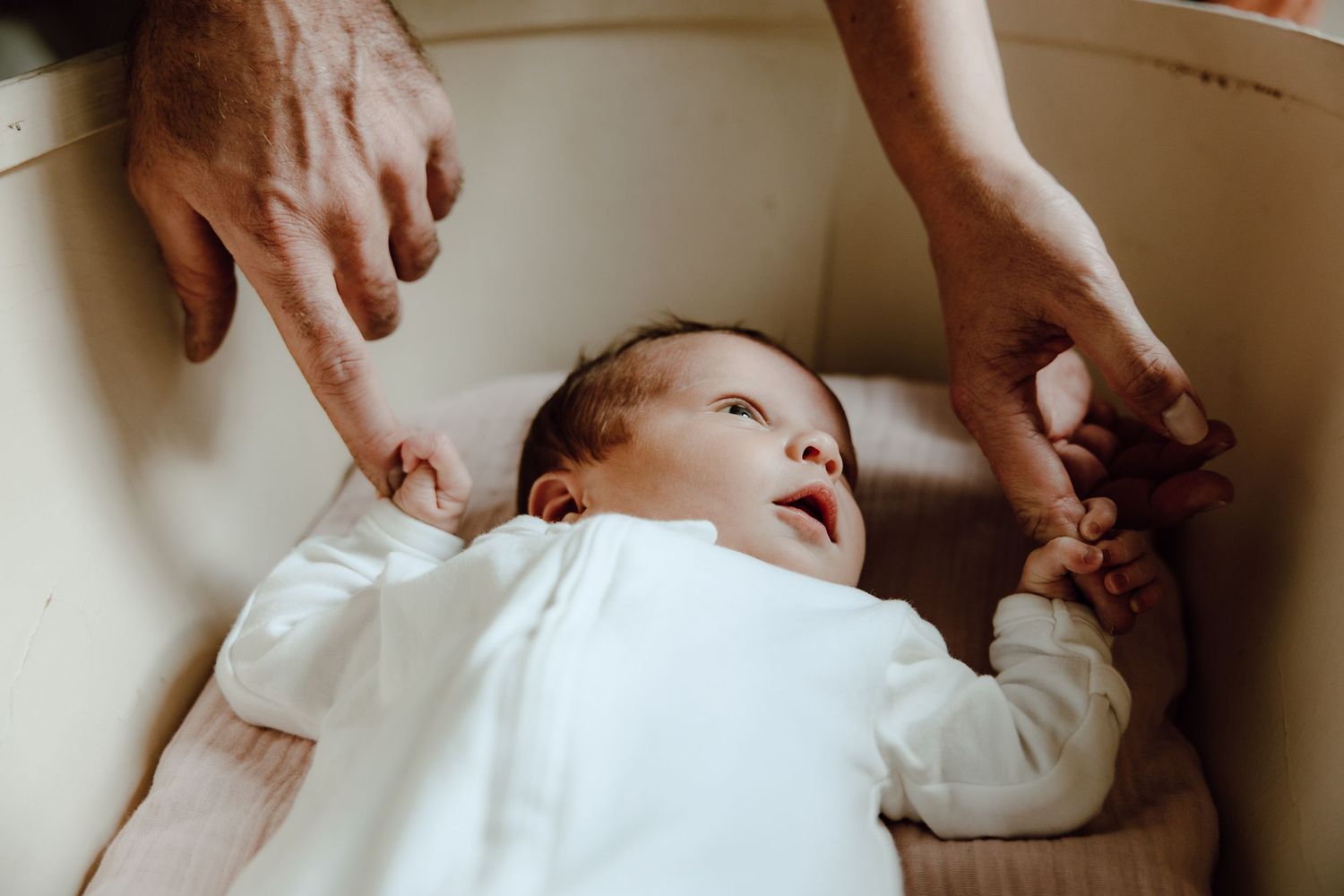 Close-up view of gentle hands caring for infant in white bedding.
