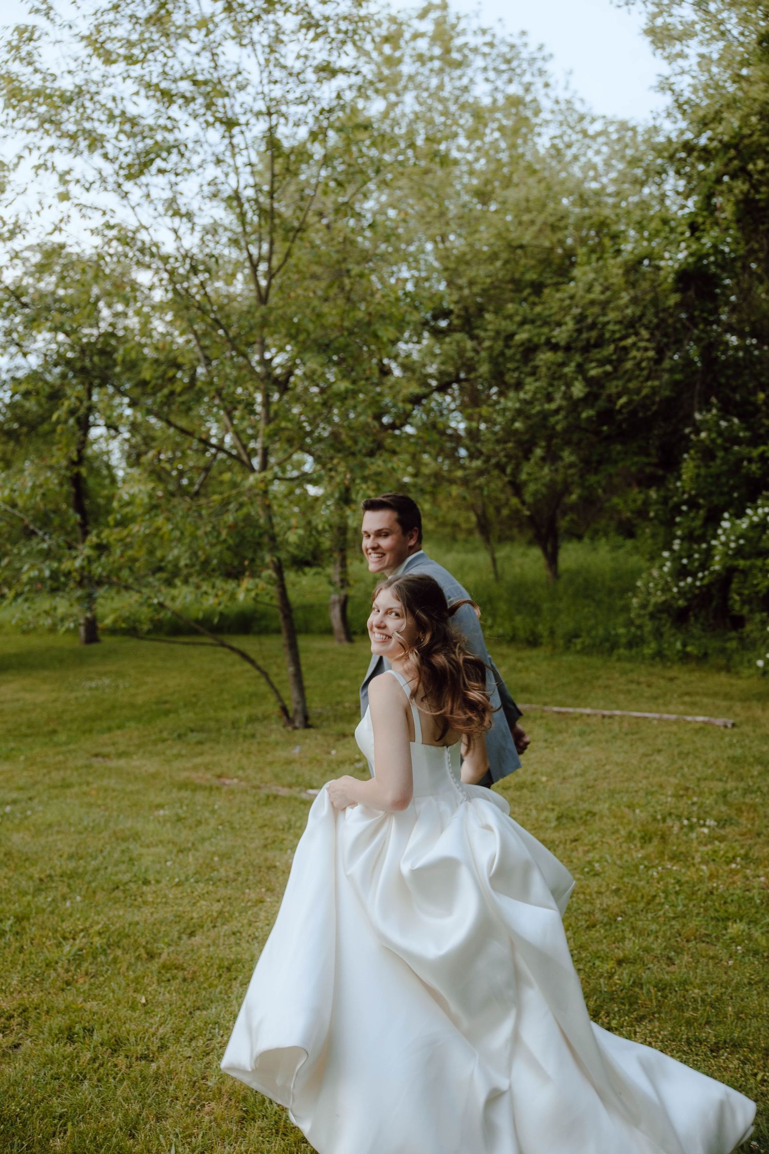 Smiling bride in white gown and groom in suit walk together through lush green garden on their wedding day.