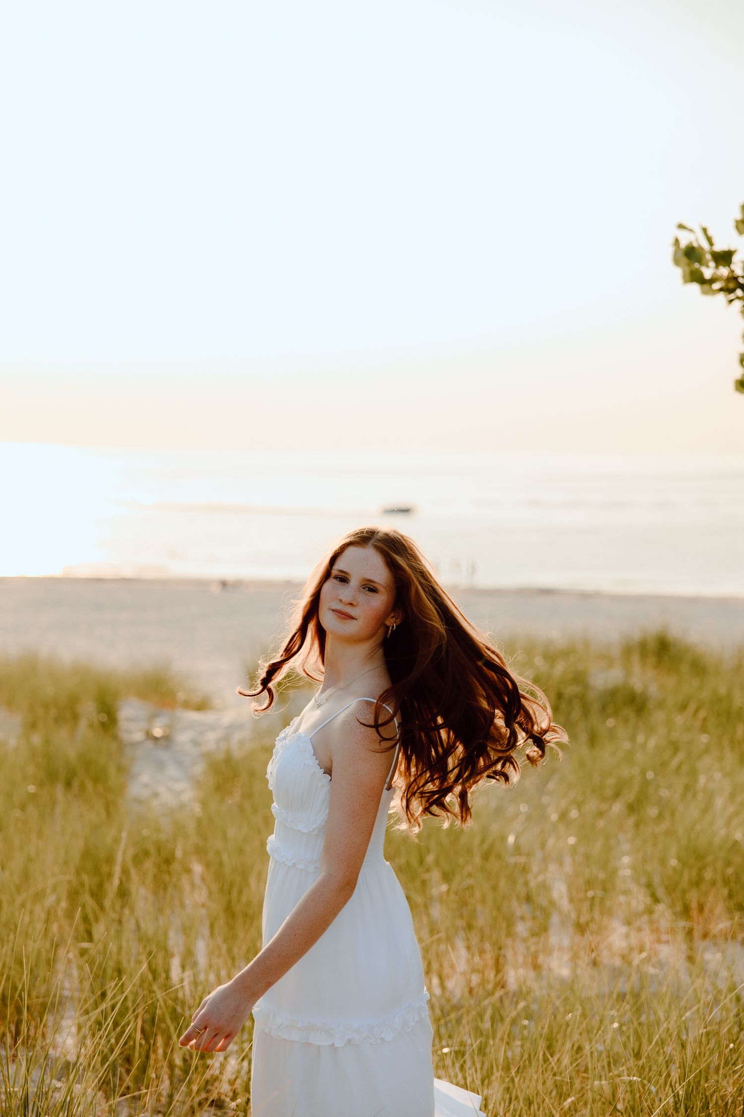Someone in a white dress twirls in a sunlit meadow during sunset.